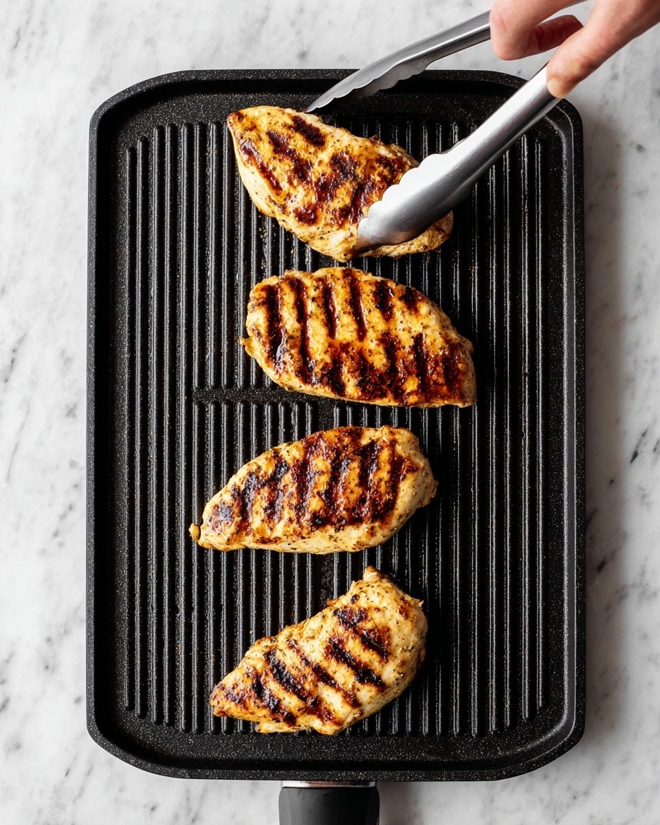 The image shows four grilled chicken pieces with dark brown grill marks on a black ridged grill pan placed on a white marbled surface. The chicken pieces are golden brown with a slightly charred texture, arranged in a vertical line on the grill pan. A pair of silver metal tongs held by a woman's hand is touching the second piece from the top, emphasizing the grilling process. The pan has a small handle cutout at the top left corner, and the contrast between the dark pan and the white marbled background highlights the cooked chicken. photo taken with an iphone --ar 4:5 --v 7