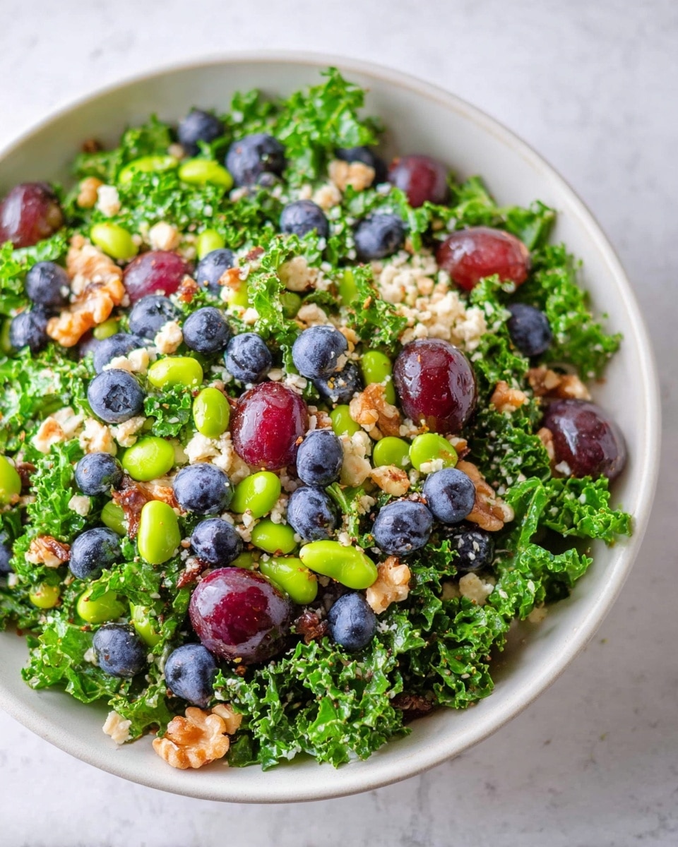 A white bowl filled with a fresh salad showing about four layers: the base layer is dark green curly kale leaves, slightly glossy and textured; scattered on top are small, round green edamame beans and light beige quinoa grains, adding small round shapes and soft texture; next are small clusters of walnut pieces and sunflower seeds, light brown with a rough texture, spread evenly; the final layer has plump, shiny red grapes and small, round dark blue blueberries, adding bright color contrast. The bowl is on a white marbled surface, and some blueberries are scattered around. Photo taken with an iphone --ar 4:5 --v 7