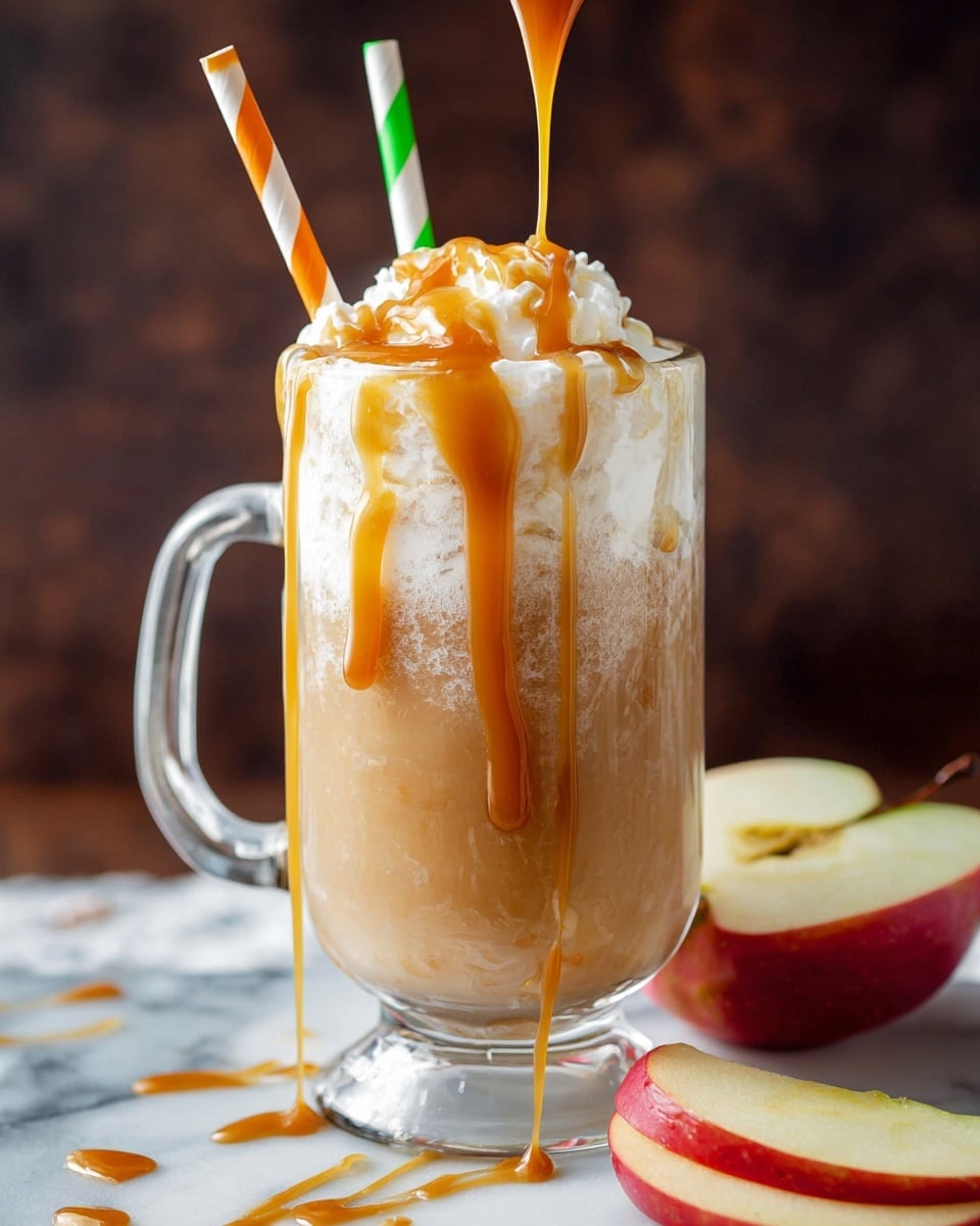 A clear glass mug with a handle is filled with a light brown drink that has a frothy white foam layer on top. Thick caramel sauce is being poured from above, dripping down the foam and edges of the mug. Two paper straws, one with green and white stripes and the other with orange and white stripes, stand inside the drink. Around the base of the mug, there are slices of red apple with cream-colored flesh placed on a white marbled surface. The background is dark and blurred, bringing focus to the drink and apples. Photo taken with an iphone --ar 4:5 --v 7