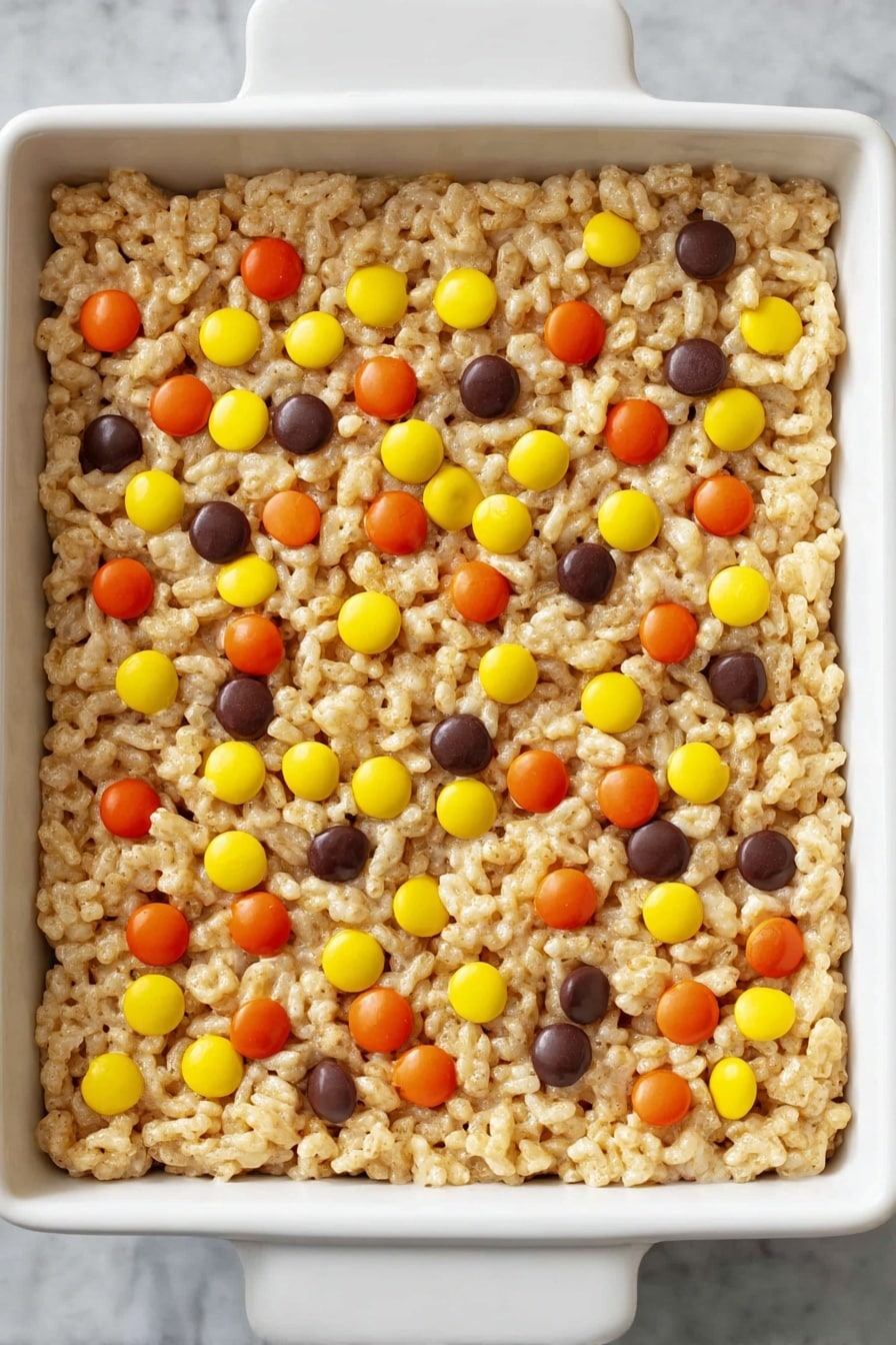 Chocolate Peanut Butter Rice Krispie Treats, peanut butter and chocolate treats, easy rice krispie treats, no-bake rice krispie recipes, nostalgic snack ideas - A single thick layer of light golden crispy puffed rice cereal mixed with melted marshmallow is pressed into a white square dish, decorated on top with scattered small round candies in bright orange, yellow, and dark brown colors. The texture of the cereal layer looks soft and sticky but holds together, and the candies are evenly spread out on the surface against a white marbled background. Photo taken with an iphone --ar 2:3 --v 7