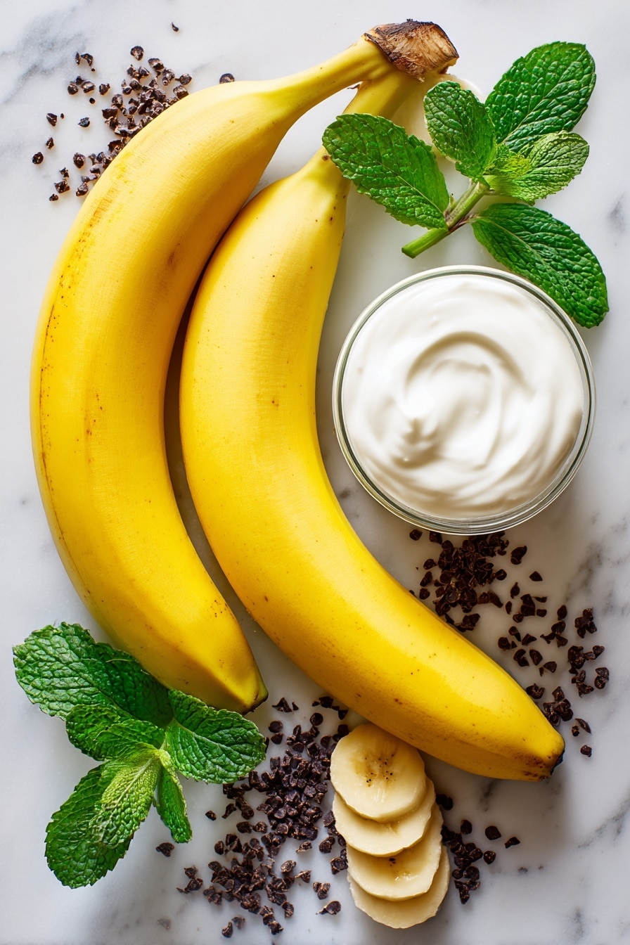 Boonanas – A Frozen Banana Ghost Halloween Treat, healthy Halloween snacks for kids, easy Halloween party treats, fun festive treat ideas, frozen banana dessert - Flat lay of two large ripe bananas with bright yellow skin, a small glass of smooth white vanilla yogurt, and scattered tiny dark mini chocolate chips with a glossy finish, all naturally arranged with a few banana slices showing their creamy texture, some fresh green mint leaves adding a pop of color, placed on white marbled surface, photo taken with an iphone --ar 2:3 --v 7