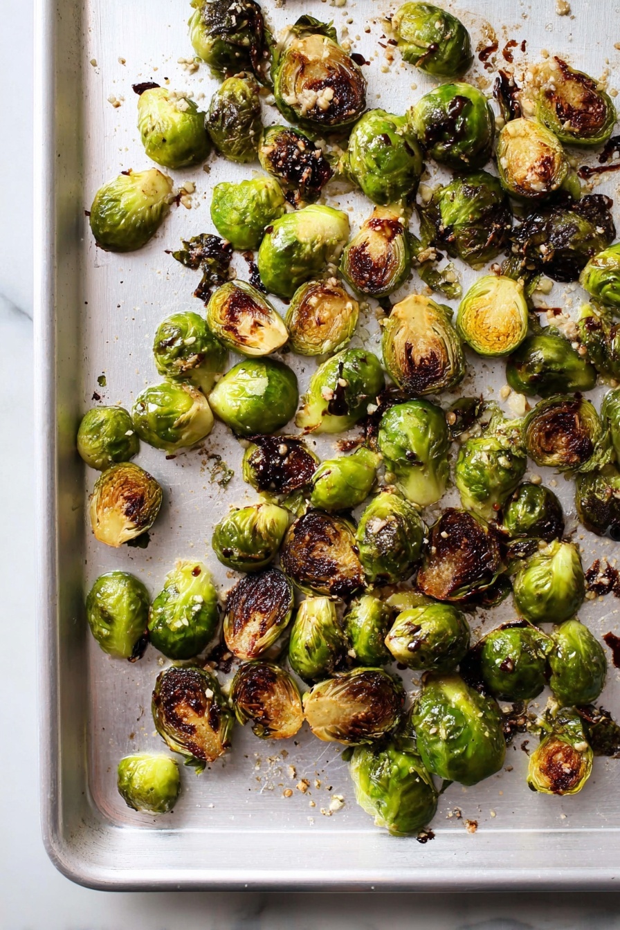 Best Roasted Brussels Sprouts, roasted Brussels sprouts, crispy Brussels sprouts, garlic roasted Brussels sprouts, healthy Brussels sprouts side dish - The image shows a single layer of roasted Brussels sprouts spread out on a white baking sheet. The Brussels sprouts are halved or quartered, with some pieces whole, and they have a mix of bright green and dark brown charred edges. Small bits of garlic and coarse salt are scattered on top, adding texture. There are also spots of dark balsamic glaze drizzled over some of the sprouts. The white baking sheet sits on a white marbled surface, with light reflecting softly on it. photo taken with an iphone --ar 2:3 --v 7