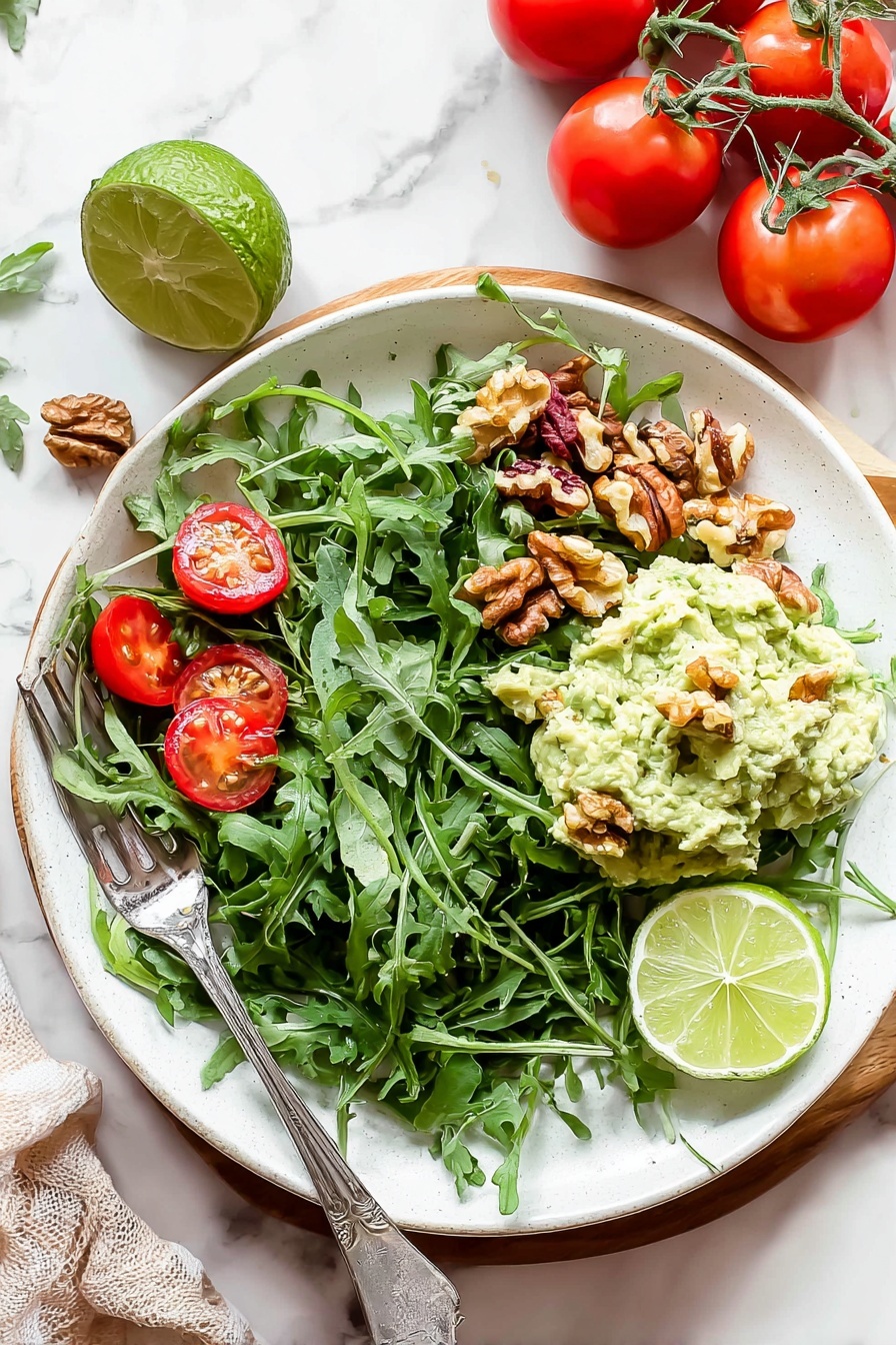 Healthy Greek Yogurt Avocado Chicken Salad, healthy chicken salad, avocado chicken salad, Greek yogurt chicken salad, light healthy lunch ideas - A white plate filled with a fresh salad on a white marbled surface. The bottom layer is a bed of dark green arugula leaves spread across the plate. Scattered on top are bright red cherry tomato halves and small brown walnut pieces. On one side, a creamy pale green mashed avocado mix is placed in a mound with a few walnut pieces on it. Two lime wedges, one light green and one yellow-green, rest on the mashed avocado. A silver fork is placed on the left side of the plate, partially resting on the salad. Nearby, whole red tomatoes on the vine and a halved lime sit on the white marbled background. Photo taken with an iphone --ar 2:3 --v 7