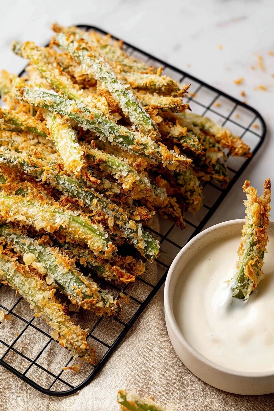 Green Bean Fries, crispy green bean snack, baked green bean sticks, healthy veggie appetizer, easy green bean side dish - The image shows many breaded green beans stacked on a black wire cooling rack on a white marbled surface with a beige cloth underneath. The beans have a crunchy, golden-brown coating with bits of light and darker browns and the green of the beans is visible under the crumbs. To the right, there is a white bowl filled with thick, creamy white dip, with two breaded green beans dipped into it. The texture of the dip is smooth and slightly shiny. Photo taken with an iphone --ar 2:3 --v 7