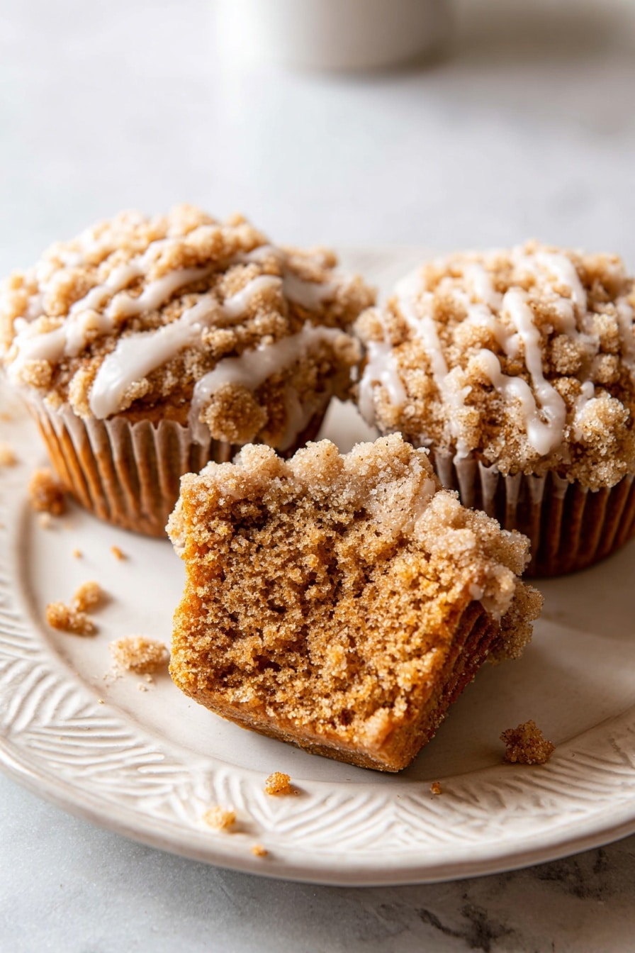 Pumpkin Crumb Cake Muffins, Pumpkin Muffin Recipes, Fall Breakfast Ideas, Easy Pumpkin Muffins, Spiced Pumpkin Baked Goods - The image shows seven golden brown muffins arranged closely on a white plate. Each muffin has a crumbly, rough-textured top layer that is light brown and covered with a light cream-colored glaze that drips down the sides in thin streaks. The muffins are placed on a smooth white marbled surface underneath the plate. Some crumbs are scattered around the plate and surface. The lighting highlights the texture and glaze shine on the muffins. Photo taken with an iphone --ar 2:3 --v 7