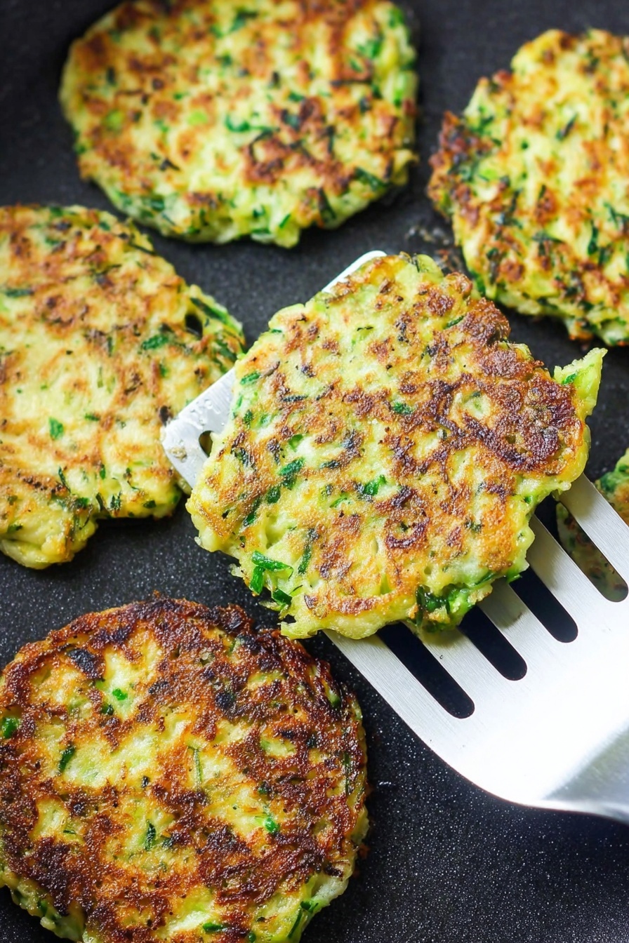 Vegan Zucchini Fritters, crispy vegan zucchini snacks, easy vegan fritters recipe, healthy zucchini side dish, plant-based zucchini appetizers - There are several flat, round fritters cooking on a black pan. Each fritter shows a mix of green herbs and light yellow batter, with crisp, dark brown patches where they have browned. One fritter is lifted by a silver spatula with long slots, showing its uneven edges and slightly rough texture. The overall look is crispy and fresh, with the green and yellow colors standing out against the pan. photo taken with an iphone --ar 2:3 --v 7
