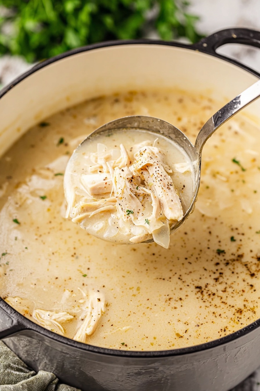 Southern Style Chicken and Dumplings, chicken and dumplings recipe, comfort food dinner, homemade chicken and dumplings, easy Southern chicken dish - A close-up view of a creamy light beige soup with shredded light tan chicken pieces mixed in. The soup has a smooth, thick texture with visible specks of black pepper spread on the surface. A shiny metal ladle lifts a portion of the soup showing the creamy broth and chicken clearly. The soup pot is white inside with a black exterior handle visible, resting on a white marbled surface with green blurred herbs in the background. Photo taken with an iphone --ar 2:3 --v 7