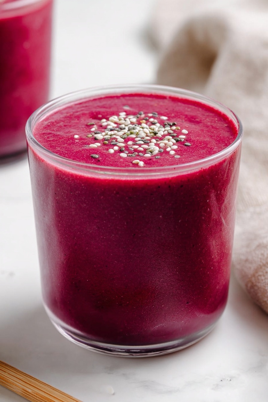 Banana Beet Smoothie, healthy smoothie with beets and bananas, nutritious beet smoothie recipe, vegan beet smoothie, energizing fruit and vegetable smoothie - A clear glass is filled with a thick, vibrant dark pink smoothie, almost reaching the top with a smooth and creamy texture. The smoothie surface is flat and topped with small white, black, and green seeds or grains sprinkled evenly across the center. The glass rests on a white marbled surface, with part of another glass filled with the same pink smoothie visible blurred in the background on the left. A light brown wooden stick lies horizontally near the base of the main glass on the left side, and a soft beige cloth is partly visible on the right side. Photo taken with an iphone --ar 2:3 --v 7