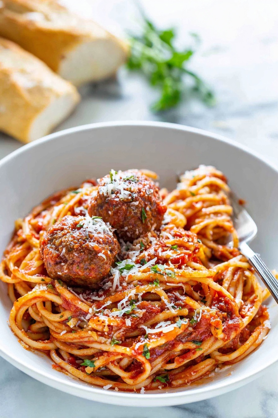 Italian Spaghetti and Meatballs, easy Italian spaghetti and meatballs, homemade spaghetti and meatballs, authentic Italian pasta dish, flavorful meatball recipe - A white bowl holds a serving of spaghetti noodles mixed with red tomato sauce, showing some herbs and seasoning. On top, there are three brown meatballs covered in sauce and sprinkled with white grated cheese. A silver fork rests inside the bowl on the right side. In the background, there is a blurred fresh green herb and some pieces of bread. The bowl sits on a white marbled surface. photo taken with an iphone --ar 2:3 --v 7