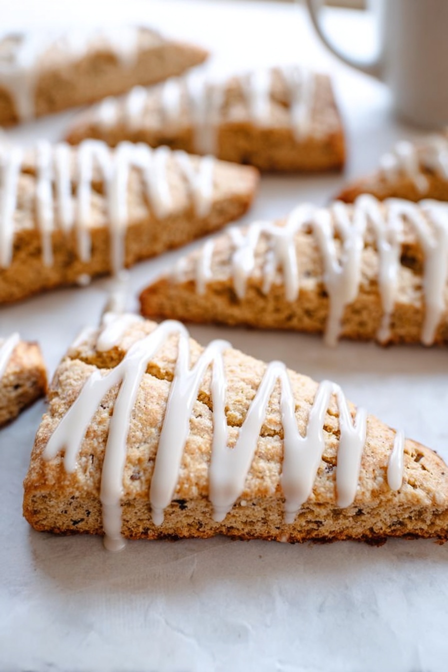Cinnamon Vanilla Biscotti, cinnamon vanilla biscotti, homemade biscotti with cinnamon and vanilla, easy biscotti recipe, crunchy vanilla cinnamon cookies - This image shows several triangular slices of light brown scones arranged on white parchment paper over a white marbled surface. Each scone slice has a visible crumbly texture with small dark specks inside. On top of each slice, there is a thick white icing drizzle applied in vertical lines, adding contrast and a smooth, glossy look to the rough texture of the scones. The focus is on a front scone slice, with others blurred in the background, giving depth to the image. photo taken with an iphone --ar 2:3 --v 7