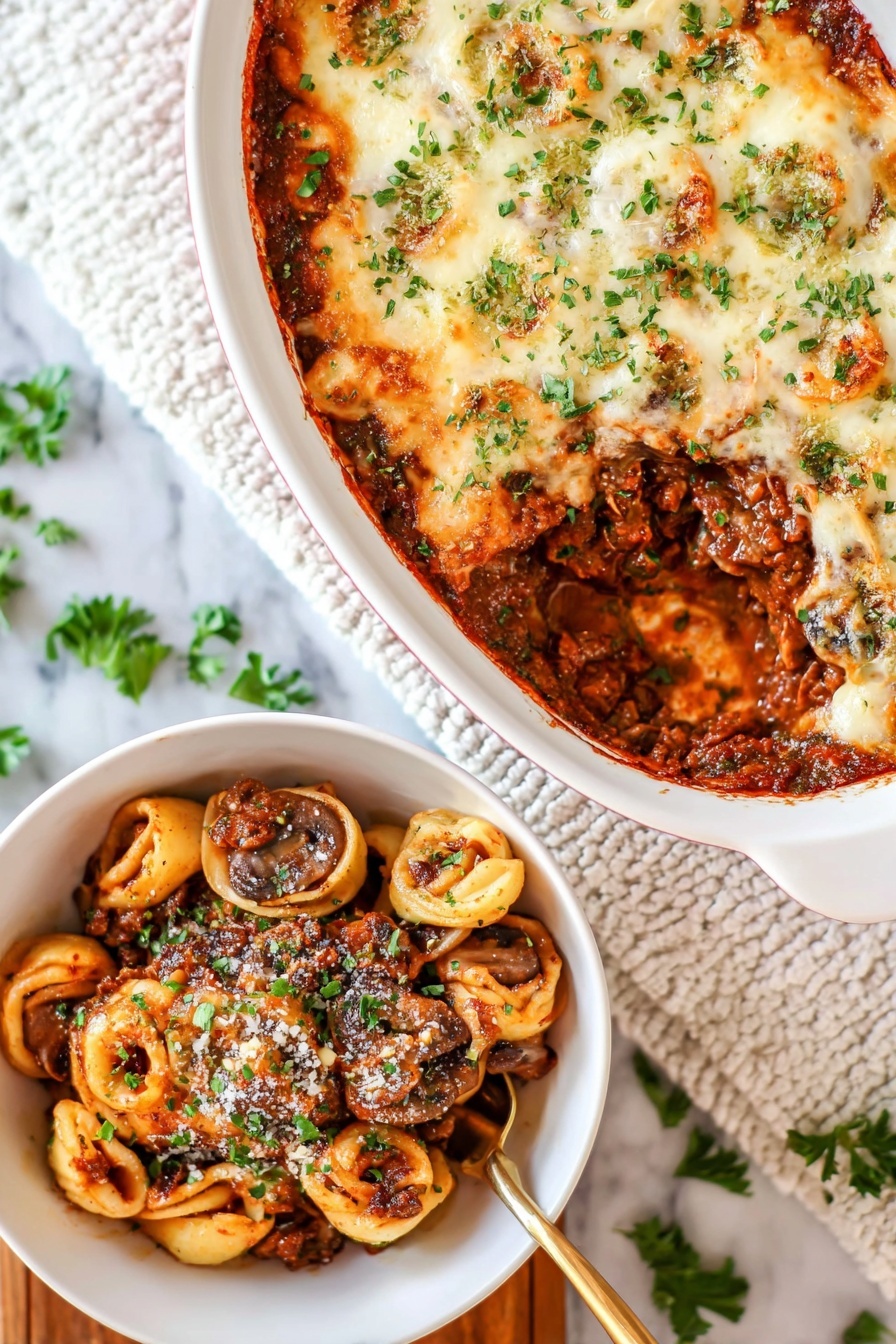 Cheesy Baked Tortellini with Ground Beef, cheesy baked tortellini, ground beef pasta bake, comfort food recipes, cheesy pasta casserole - The image shows a white oval baking dish with a layered casserole on a white marbled surface. The top layer is melted, lightly browned cheese sprinkled with green herbs. A section is scooped out, revealing a rich, dark brown meat sauce mixed with whole mushrooms and tortillas shaped like small circles inside the dish. Next to it is a white bowl filled with a serving of the casserole, showing layers of browned meat sauce, mushrooms, and pasta circles, all topped with some grated cheese and chopped green herbs. A golden spoon is partially visible in the bowl. The background includes a white textured cloth and scattered green herb leaves. photo taken with an iphone --ar 2:3 --v 7
