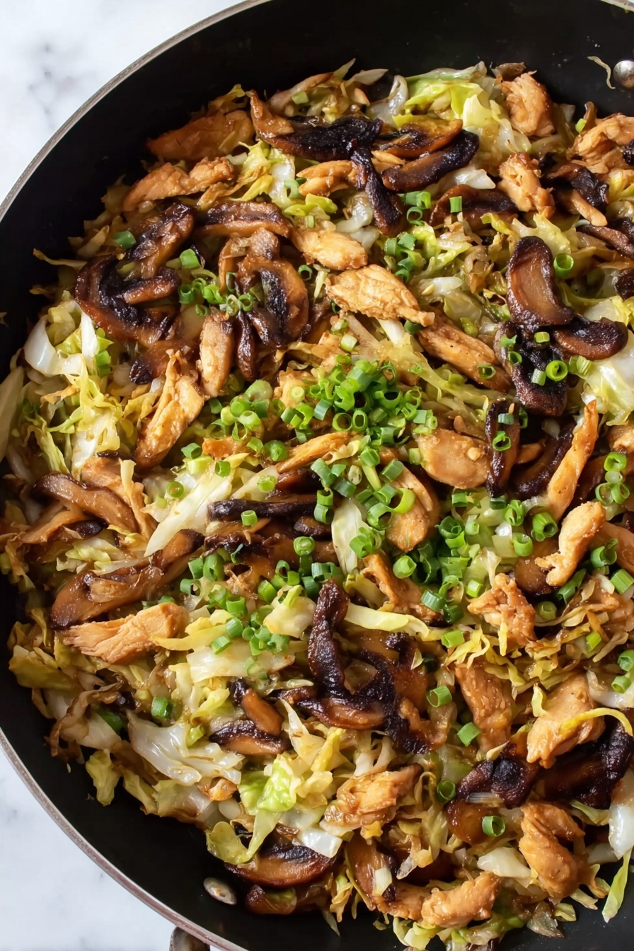 Moo Shu Chicken, Moo Shu Chicken recipe, Chinese chicken stir-fry, quick Asian dinner, easy Chinese chicken dish - The image shows a close-up of a black pan filled with a stir-fry dish. The dish has many layers: on the bottom are thin, light green and white strips of cooked cabbage, mixed with pale yellow thin strips that look like fried tofu or egg. Above this layer are medium brown grilled mushroom slices with a slightly shiny texture. On top of that are small pieces of golden brown cooked chicken mixed evenly throughout. Scattered over the top are small, bright green chopped spring onions. The black pan is placed on a white marbled surface. Photo taken with an iphone --ar 2:3 --v 7