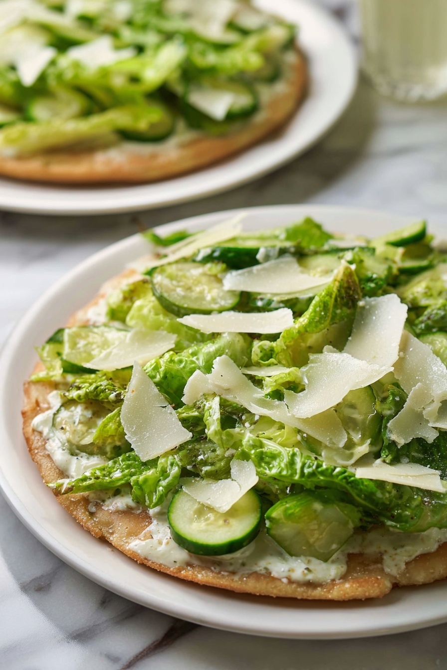 Chicken Caesar Salad Pizza, Chicken Caesar Salad Pizza with Crispy Crust, Caesar salad pizza, crispy chicken crust pizza, unique pizza recipes - The dish shows a flat round base with a light brown, slightly crispy texture. On top of the base, there is a layer of creamy white sauce spreading evenly. Above the sauce, there is a thick layer of green romaine lettuce pieces, mixed with round slices of light green cucumber scattered on top. Thin, irregular white shavings, likely cheese, are spread across the green vegetables. The dish is served on a simple white plate placed on a white marbled surface, with another similar dish visible blurred in the background. photo taken with an iphone --ar 2:3 --v 7
