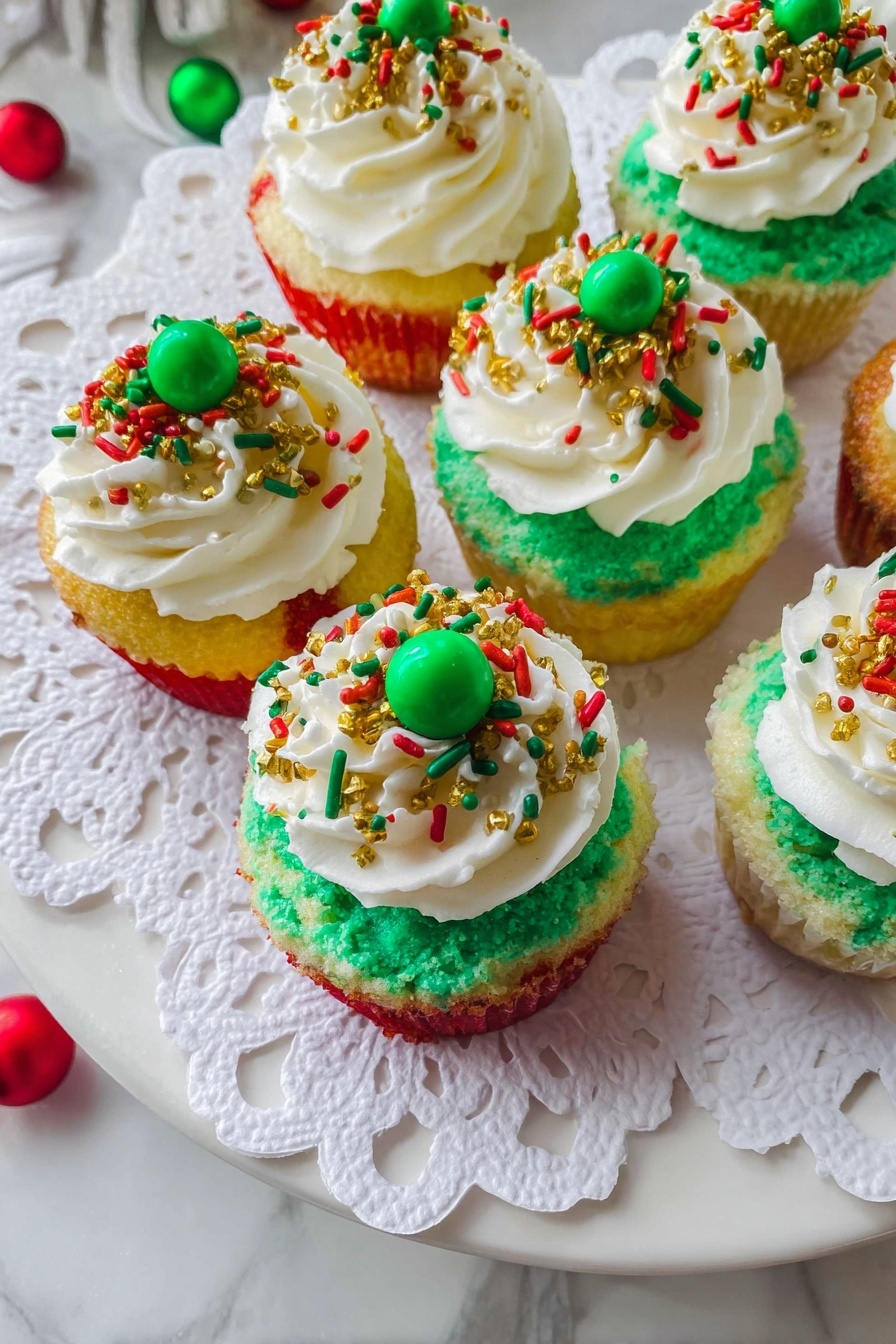 Mini Christmas Oreo Cheesecakes, Christmas dessert ideas, easy holiday cheesecake, cute festive treats, no-bake mini cheesecakes - The image shows six cupcakes placed on a white plate covered with a white paper doily. Each cupcake has three visible layers of cake with red, yellow, and green colors, stacked one on top of another. On top of the cake layers is a thick layer of green frosting spread evenly. Over this green frosting, there is a generous swirl of white whipped cream. The whipped cream is decorated with holiday-themed sprinkles in red, green, and gold, including small rods, round dots, and tiny gold balls. Two cupcakes have a green candy ball placed in the center on top of the whipped cream. The plate is set on a white marbled surface with some colorful decorations partially visible around the edges. photo taken with an iphone --ar 2:3 --v 7