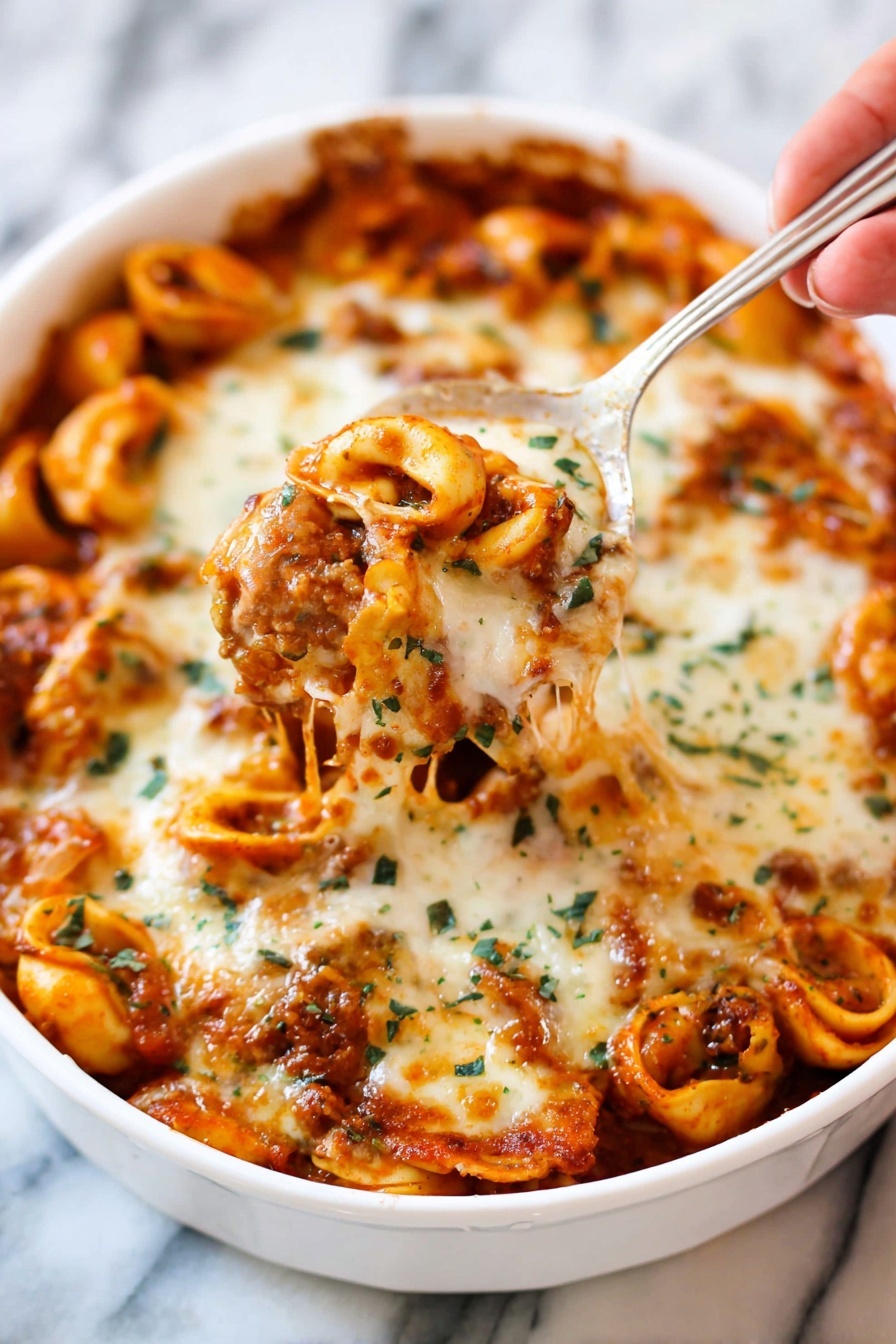 Cheesy Baked Tortellini with Ground Beef, cheesy baked tortellini, ground beef pasta bake, comfort food recipes, cheesy pasta casserole - A white dish filled with baked tortellini pasta tossed in a rich red tomato sauce and covered with a thick layer of melted, golden-brown cheese with green herb sprinkles on top. Some tortellini are visible under the cheese, showing their smooth curved shapes and orange sauce coating. A woman's hand holds a silver spoon lifting a portion of the cheesy pasta, with melted cheese stretching slightly. The background shows more pasta inside the white dish on a white marbled surface. photo taken with an iphone --ar 2:3 --v 7