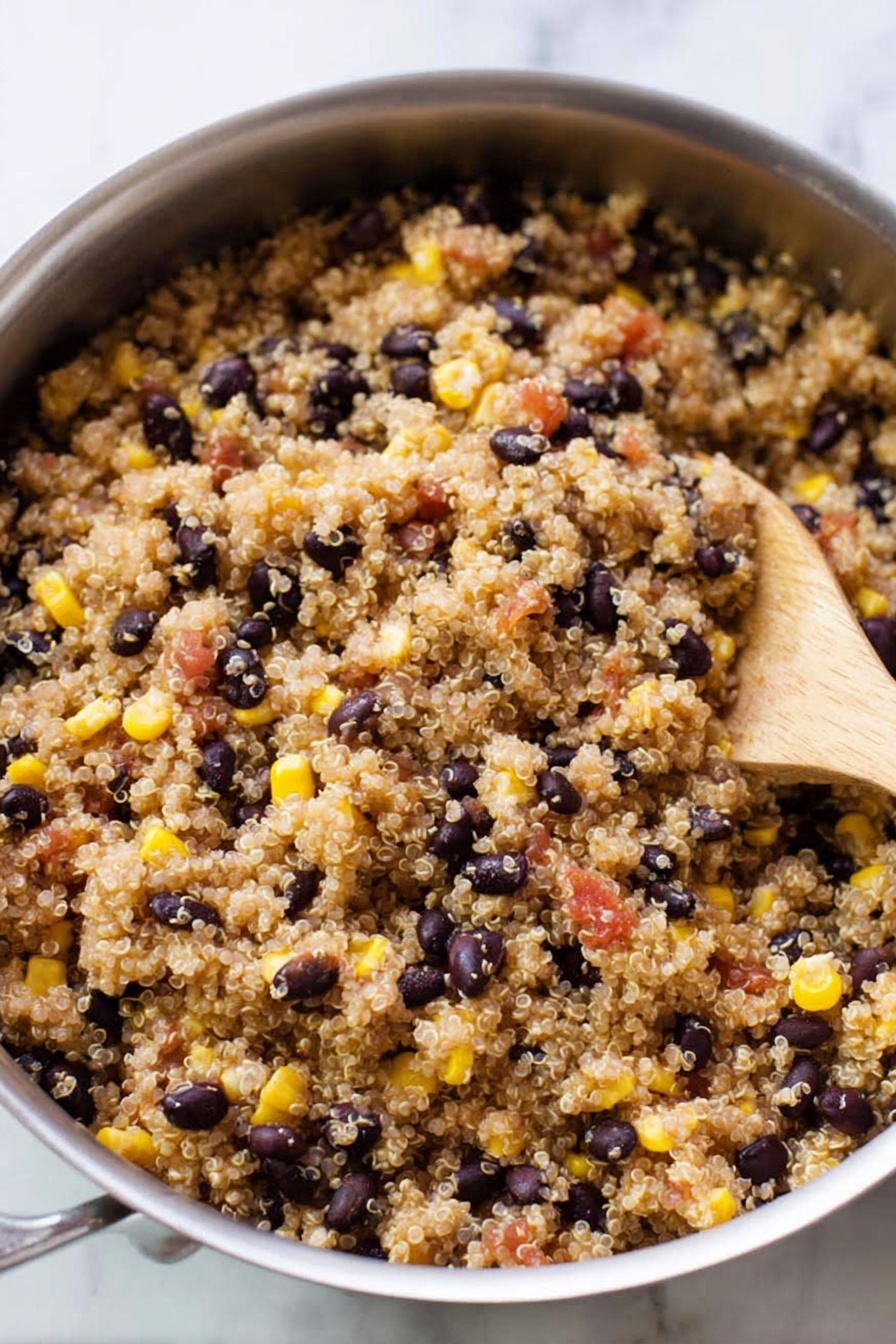 Mexican Quinoa Bowl, easy Mexican quinoa recipe, healthy quinoa bowls, quick Mexican meal, nutritious quinoa dinner - A silver pan filled with cooked quinoa mixed with black beans, yellow corn, and small pieces of red tomatoes. The quinoa grains are light brown and fluffy, evenly spread throughout the pan. The black beans are scattered, showing their dark smooth texture while the yellow corn adds bright pops of color. A wooden spoon rests inside the pan on the right side, partially covered by the quinoa mixture. The background is a white marbled surface. photo taken with an iphone --ar 2:3 --v 7