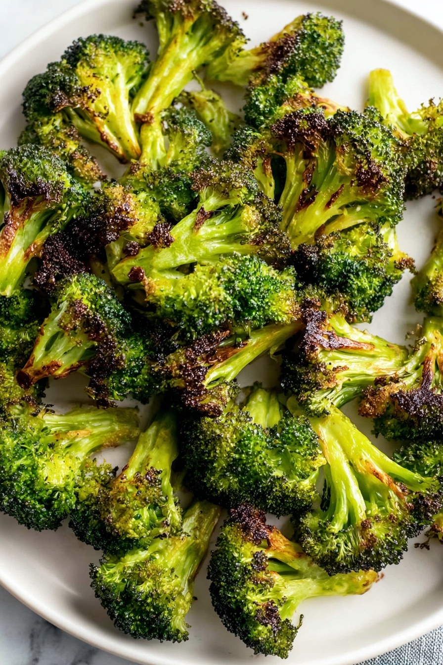 Oven Roasted Broccoli with Garlic and Paprika, roasted broccoli side dish, healthy roasted broccoli, easy vegetable side, flavorful broccoli recipe - A white round plate is filled with many pieces of roasted broccoli. Each broccoli piece shows a bright green color with dark brown, crispy edges where it is roasted. The broccoli is scattered all over the plate, with some pieces standing up and others lying flat, showing their textured tops and thick stalks. The plate is placed on a white marbled surface. photo taken with an iphone --ar 2:3 --v 7