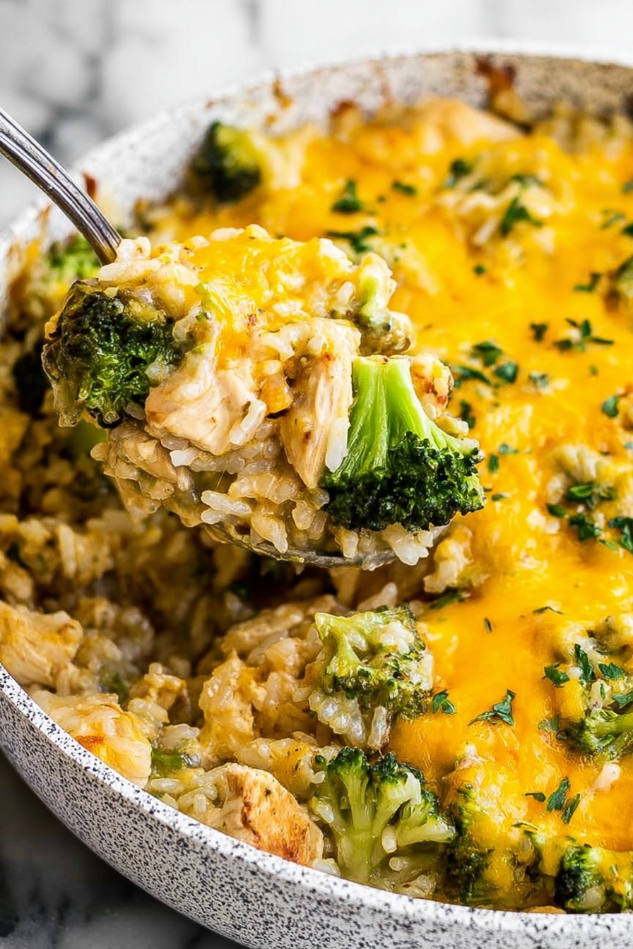 One Pot Cheesy Chicken Broccoli Rice Bake, cheesy chicken broccoli rice casserole, easy one pot chicken and rice recipe, creamy broccoli chicken bake, quick comforting dinner - The image shows a close-up of a dish in a white speckled pan filled with a cheesy mixture. The dish has two main layers: at the bottom, tender pieces of light brown chicken mixed with white rice; on top, bright green broccoli florets are scattered evenly. A thick layer of melted yellow cheese covers the whole dish, with some green herbs sprinkled on top. A metal spoon lifts a portion, showing the mix of chicken, rice, broccoli, and cheese together. The background is a white marbled texture. Photo taken with an iphone --ar 2:3 --v 7