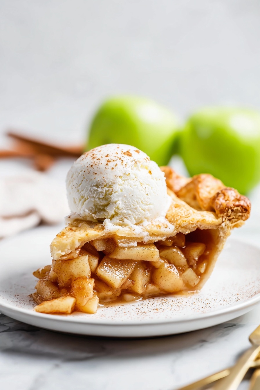 Vegan Pear Chai Spice Pie, vegan pear pie with chai spices, cozy vegan dessert recipes, plant-based fruit pie, vegan holiday dessert - A slice of apple pie sits on a white plate, showing three main layers: the bottom crust is golden brown and slightly flaky, the middle layer is filled with soft, cinnamon-spiced apple pieces that look juicy and tender, and the top crust is also golden with a slight sprinkle of sugar. On top of the pie slice is a round scoop of white ice cream with a light dusting of cinnamon. The plate rests on a white marbled surface, and in the background, out of focus, two green apples and a fork and knife are visible. Photo taken with an iphone --ar 2:3 --v 7