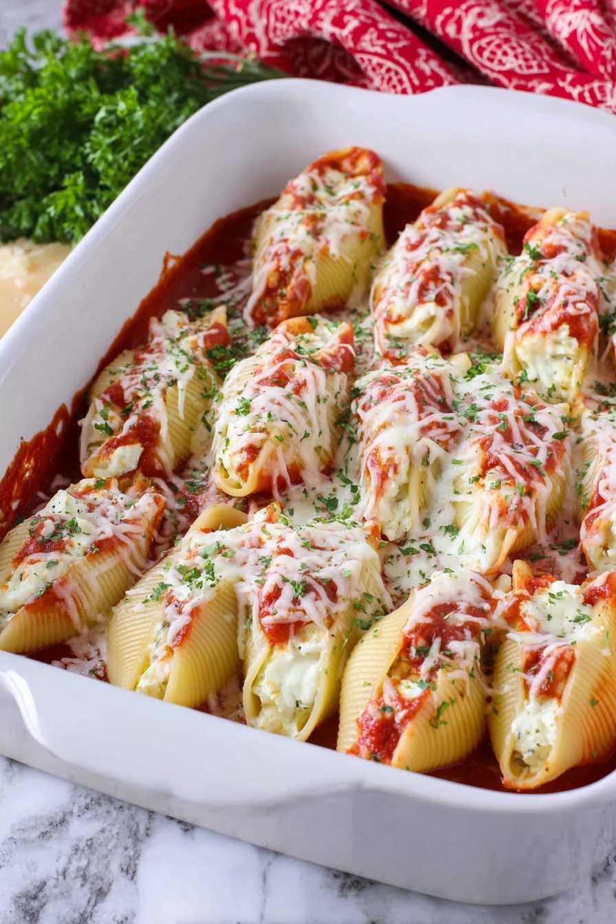 Cheesy Chicken Stuffed Shells, stuffed shell pasta, cheesy chicken dinner, baked stuffed shells, easy Italian stuffed shells - The image shows a white baking dish filled with two layers of large pasta shells. The bottom layer is covered with a red tomato sauce, and the shells are stuffed with white cheese inside, visible in some openings. The top layer consists of more pasta shells placed closely next to each other, covered with melted white cheese sprinkled with green herbs and bits of red tomato sauce. The dish is placed on a white marbled surface, with some green herbs and a red patterned cloth in the background. Photo taken with an iphone --ar 2:3 --v 7