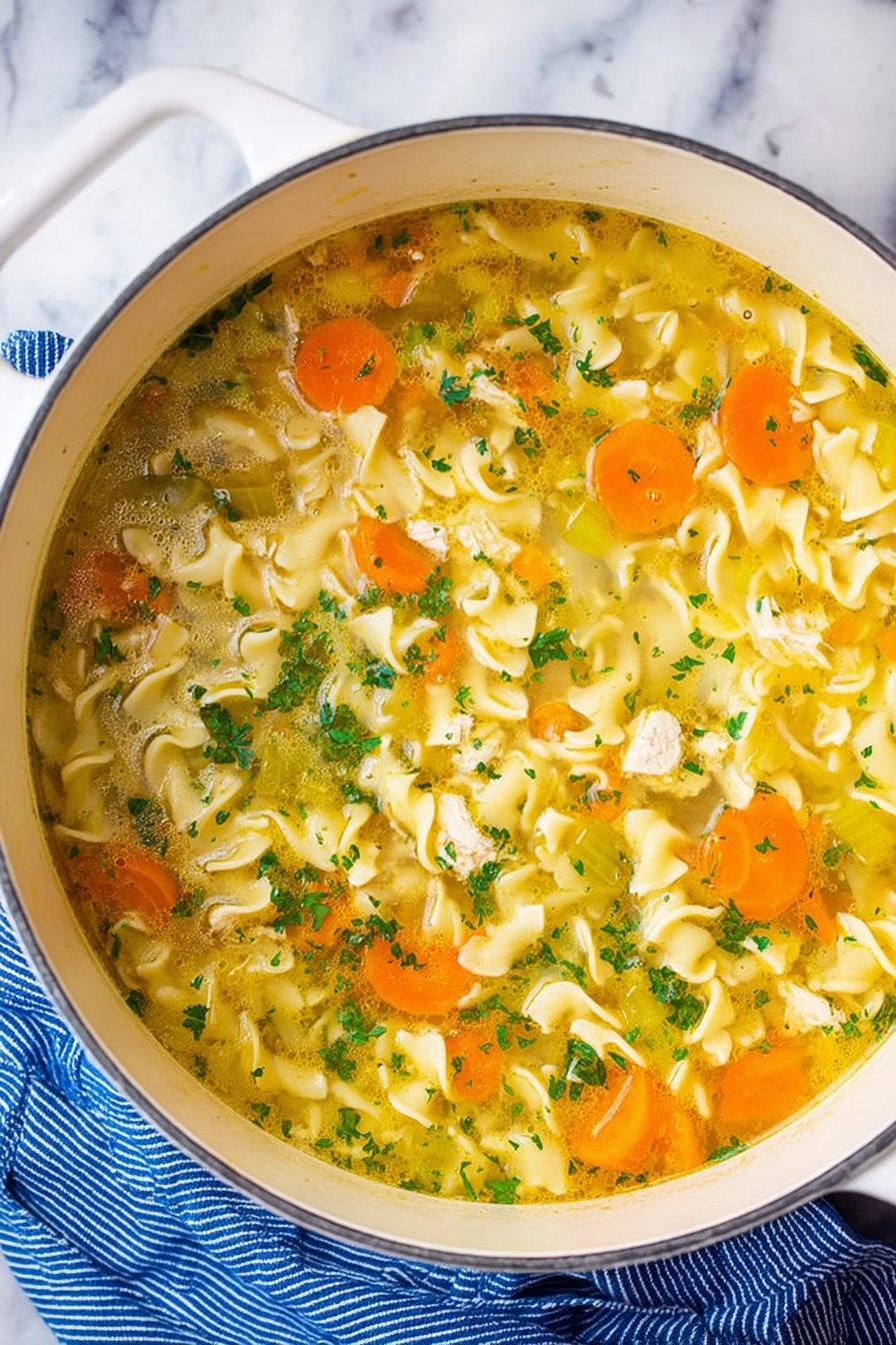 Vegan Chicken Noodle Soup, vegan noodle soup, plant-based chicken soup, vegan comforting soup, dairy-free chicken noodle soup - A white pot filled with clear yellow broth soup containing wavy egg noodles that float through the liquid. Slices of bright orange carrots and pale green celery are mixed evenly throughout the soup, along with small pieces of white chicken. The soup is topped with finely chopped fresh green herbs, adding small bursts of color. The pot is resting on a white marbled surface next to a blue striped cloth. Photo taken with an iphone --ar 2:3 --v 7