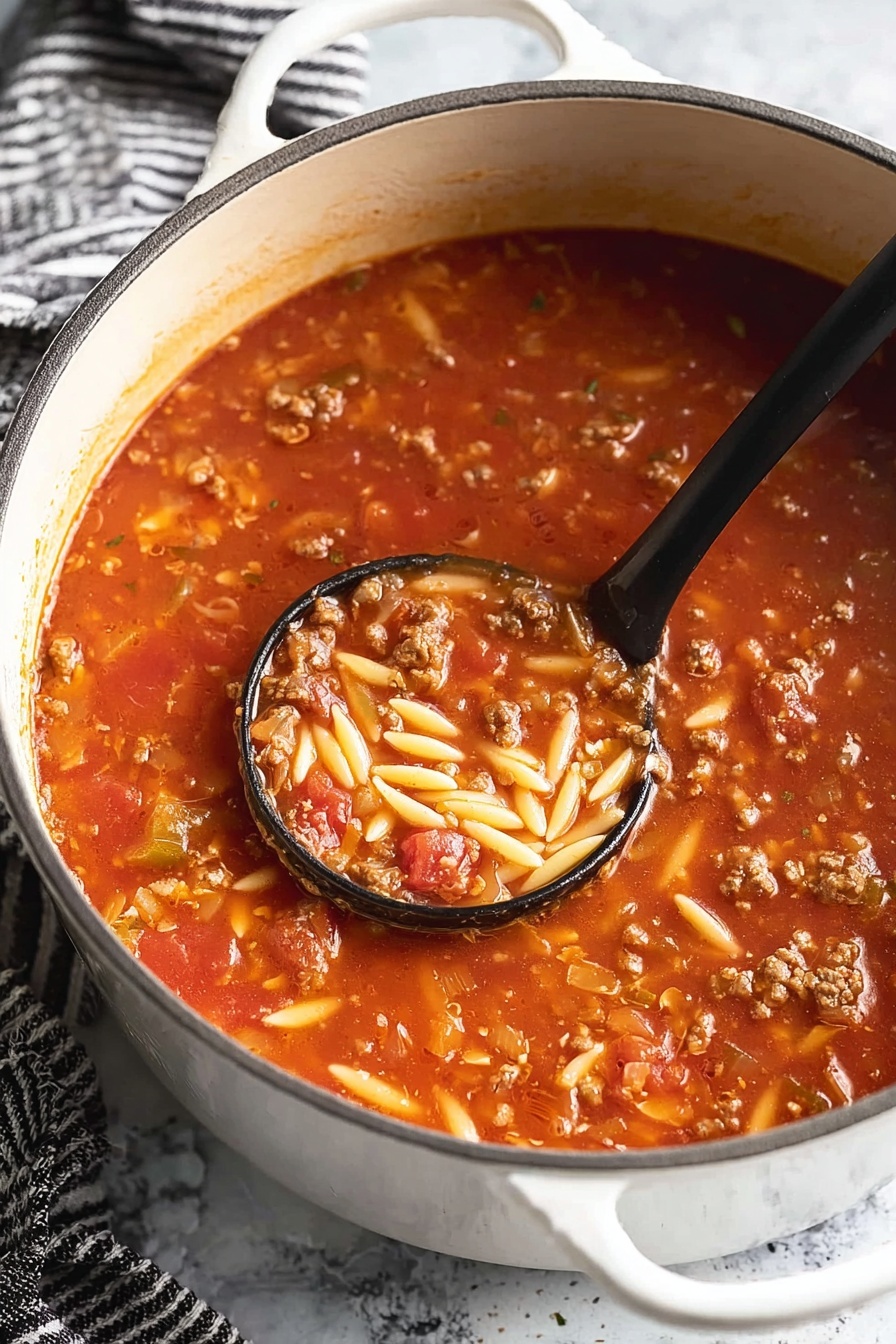 Italian Sausage Soup with Orzo, Italian Sausage Soup, hearty sausage and orzo soup, quick Italian sausage soup, comforting sausage soup recipe - A white pot filled with a thick tomato soup that has three visible layers: a bright red tomato base with a smooth texture, mixed with small chunks of cooked ground meat in brown color, and short, oval-shaped pieces of light yellow pasta scattered throughout. A black ladle scoops some soup near the center, showing all three layers together with a shiny, moist texture. The pot is on a white marbled surface with a black-and-white striped cloth nearby. Photo taken with an iphone --ar 2:3 --v 7