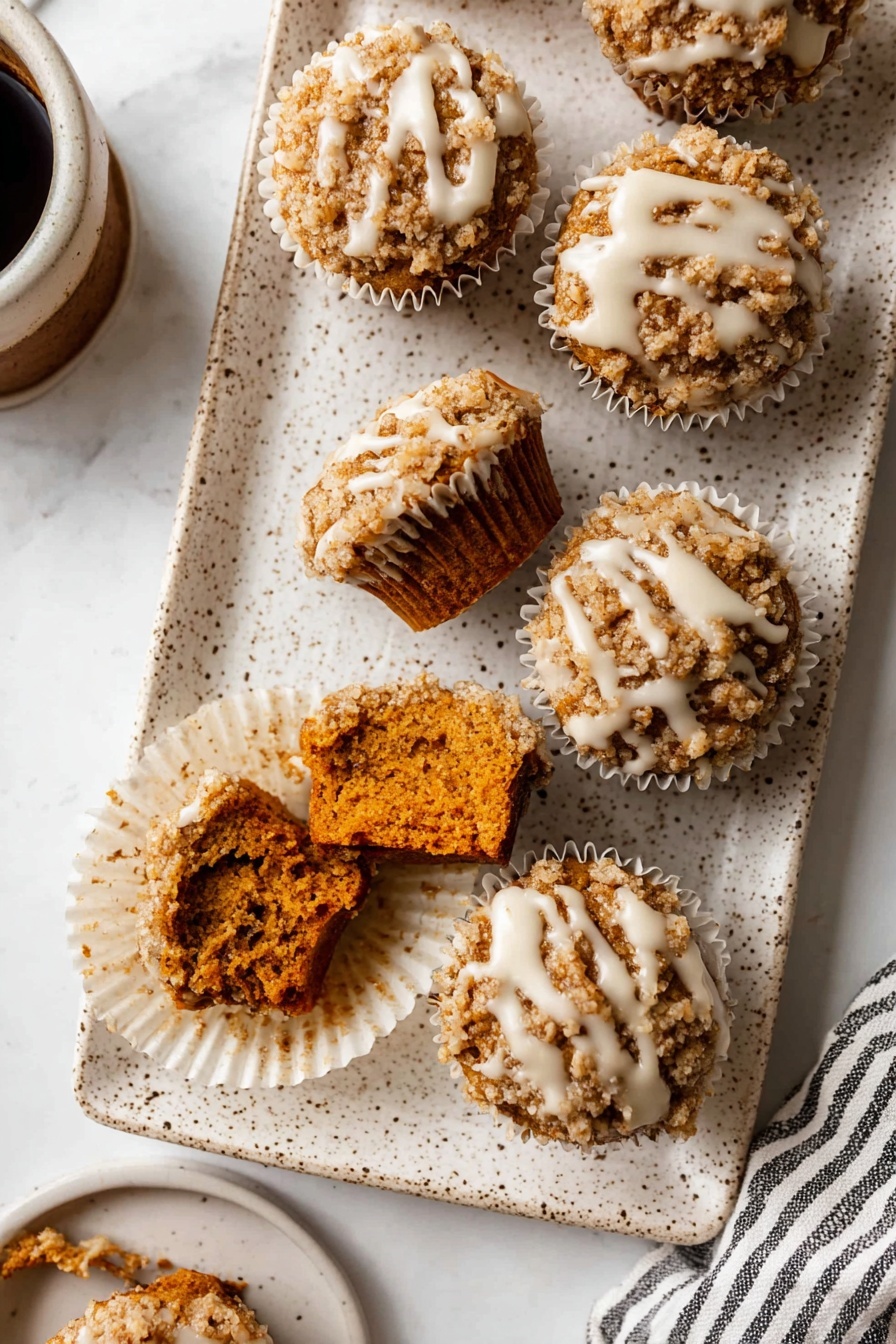 Pumpkin Crumb Muffins with Maple Icing, pumpkin muffin recipes, autumn pumpkin muffins, maple icing bakery treats, cozy fall muffin ideas - The image shows a white speckled rectangular plate holding seven small muffins with crumbly tops. Each muffin has a rough, light brown crumb layer with a drizzle of white icing over it. Two muffins in the front have bites taken out, showing a dense, dark orange interior. The muffins sit inside white paper liners arranged close to each other. The plate is on a white marbled textured surface with part of a cup of coffee and a striped cloth visible on the edges. photo taken with an iphone --ar 2:3 --v 7