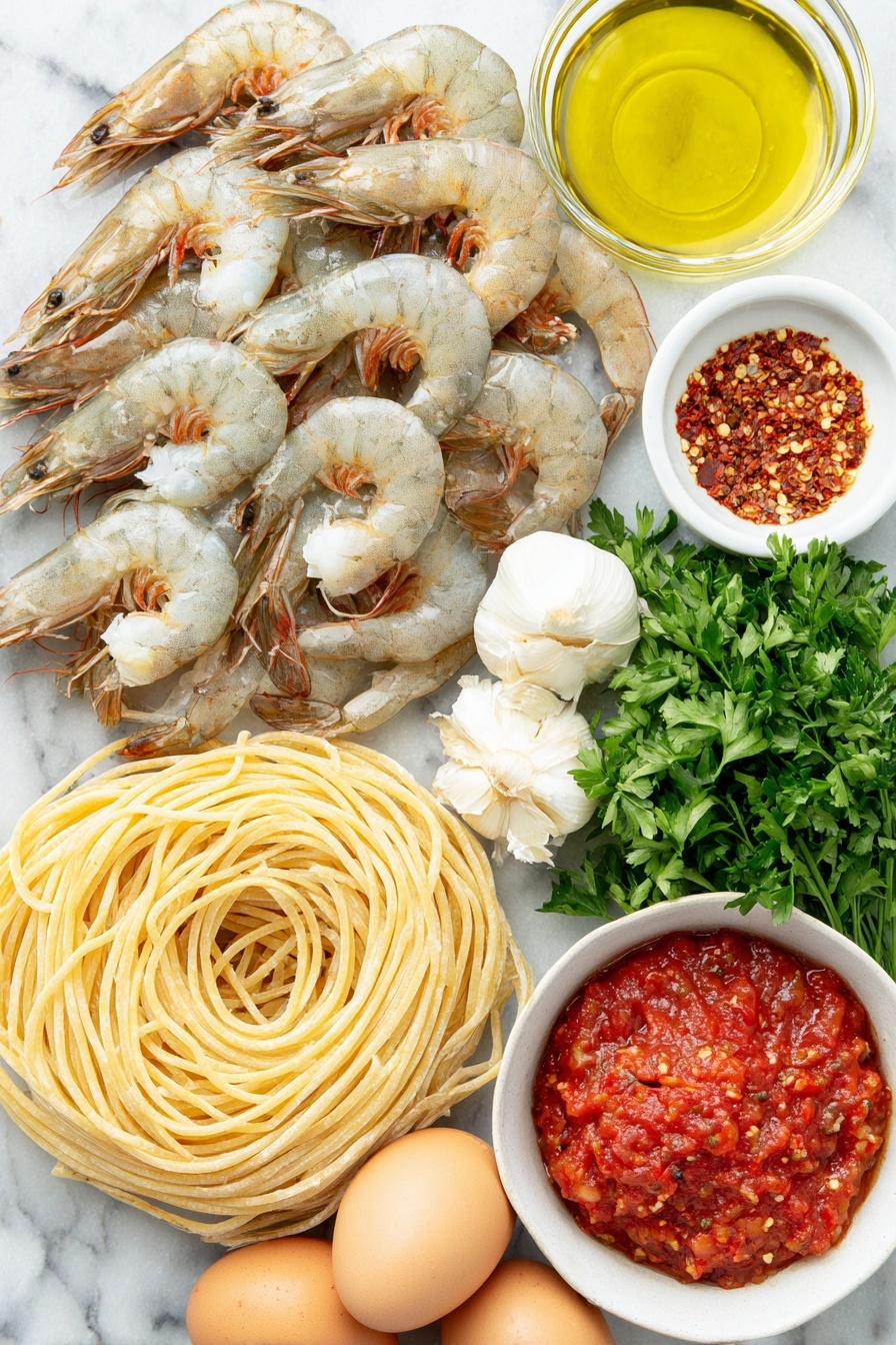 Shrimp Fra Diavolo Pasta, spicy shrimp pasta, quick seafood pasta recipe, Italian shrimp pasta, flavorful shrimp pasta dish - Flat lay of dry linguine pasta neatly coiled, plump large shrimp with tails on arranged in a gentle curve, a small white bowl filled with shiny olive oil, a small white bowl containing bright red Calabrian chili paste, a cluster of fresh garlic cloves with papery skins intact, a small white bowl of vivid red crushed San Marzano tomatoes, fresh vibrant green parsley sprigs artistically placed, a small white bowl holding mixed red pepper flakes, and three whole uncracked brown eggs arranged symmetrically, all placed on a clean white marble surface, soft natural light, photo taken with an iPhone, professional food photography style, fresh ingredients, white ceramic bowls, no bottles, no duplicates, no utensils, no packaging --ar 2:3 --v 7 --p m7354615311229779997