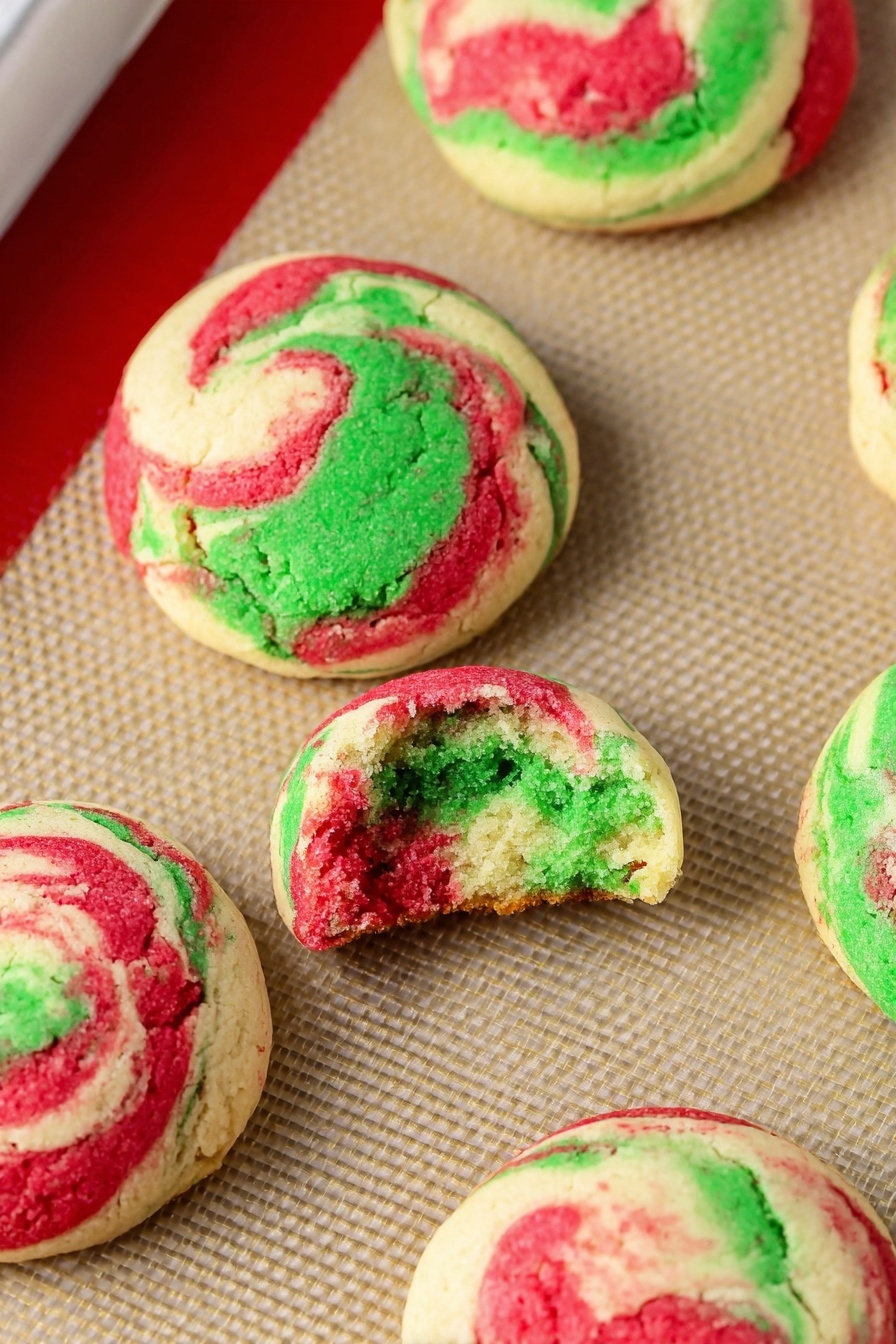 Christmas Cheesecake Cookies, holiday cheesecake cookies, festive cheesecake cookies, peppermint cheesecake cookies, marbled holiday cookies - This image shows a baking tray lined with a beige silicone mat that holds eight round cookie dough balls. Each ball has three swirled colors: green, red, and white, giving a marbled effect. The dough balls are spaced evenly, with a slightly rough texture on top and smooth sides. The tray has a silver metal edge and a red silicone border around the baking mat. The background is a white marbled texture. photo taken with an iphone --ar 2:3 --v 7