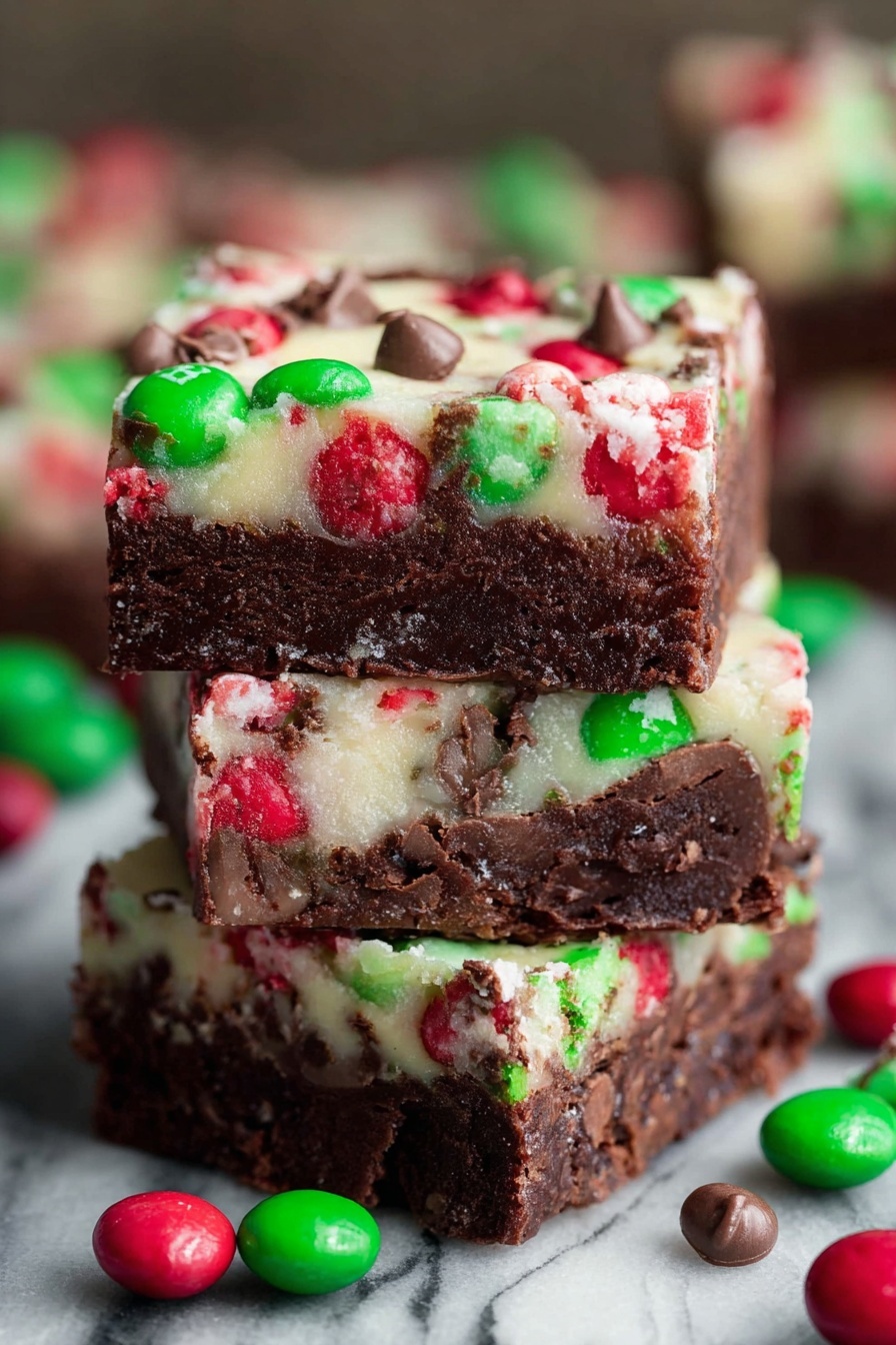 Christmas Magic Layer Brownie Bars, festive holiday brownie bars, Christmas dessert recipes, layered brownie recipe for Christmas, holiday treat ideas - The image shows a close-up of three stacked dessert bars with two clear layers. The bottom layer is thick, dense, and dark brown with a fudgy texture. The top layer is thinner and creamy white, embedded with red and green candy pieces and small chocolate chunks scattered throughout. Around the stack, several red and green round candies with a shiny shell are scattered. The background has a white marbled texture. photo taken with an iphone --ar 2:3 --v 7