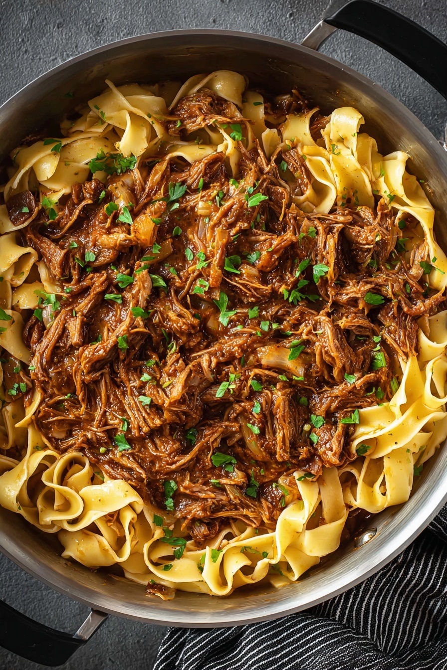 Short Rib Ragu with Pasta, hearty beef ragu, slow-cooked beef pasta, comforting Italian meat sauce, tender short rib pasta dish - The image shows a close-up of a pan filled with two main layers: the bottom layer is flat, wide pasta noodles in a pale yellow color, and the top layer is shredded meat cooked in a rich brown sauce. The shredded meat is mixed with small, finely chopped green herbs scattered evenly over the dish, adding spots of bright green color. The pan is metallic and round, resting on a dark gray surface with a striped black and white cloth visible at the bottom right. The overall look is hearty and rustic with a mix of smooth noodles and textured meat. photo taken with an iphone --ar 2:3 --v 7