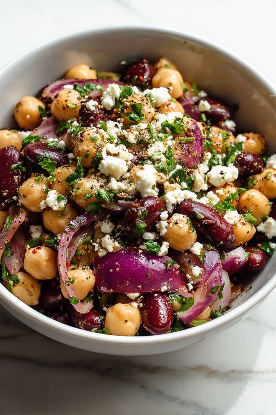 Chickpea Black Bean Salad, Chickpea Black Bean Salad recipe, healthy chickpea black bean salad, easy vegetarian bean salad, protein-rich bean salad - A white bowl filled with a salad showing three main layers: the bottom layer is a mix of beige chickpeas and dark red kidney beans; the middle layer includes large pieces of purple-red onion; the top layer is sprinkled with white crumbled cheese and small bits of bright green parsley, all mixed with visible black pepper and seasoning specks. The salad looks fresh and colorful, sitting on a white marbled surface, photo taken with an iphone --ar 2:3 --v 7