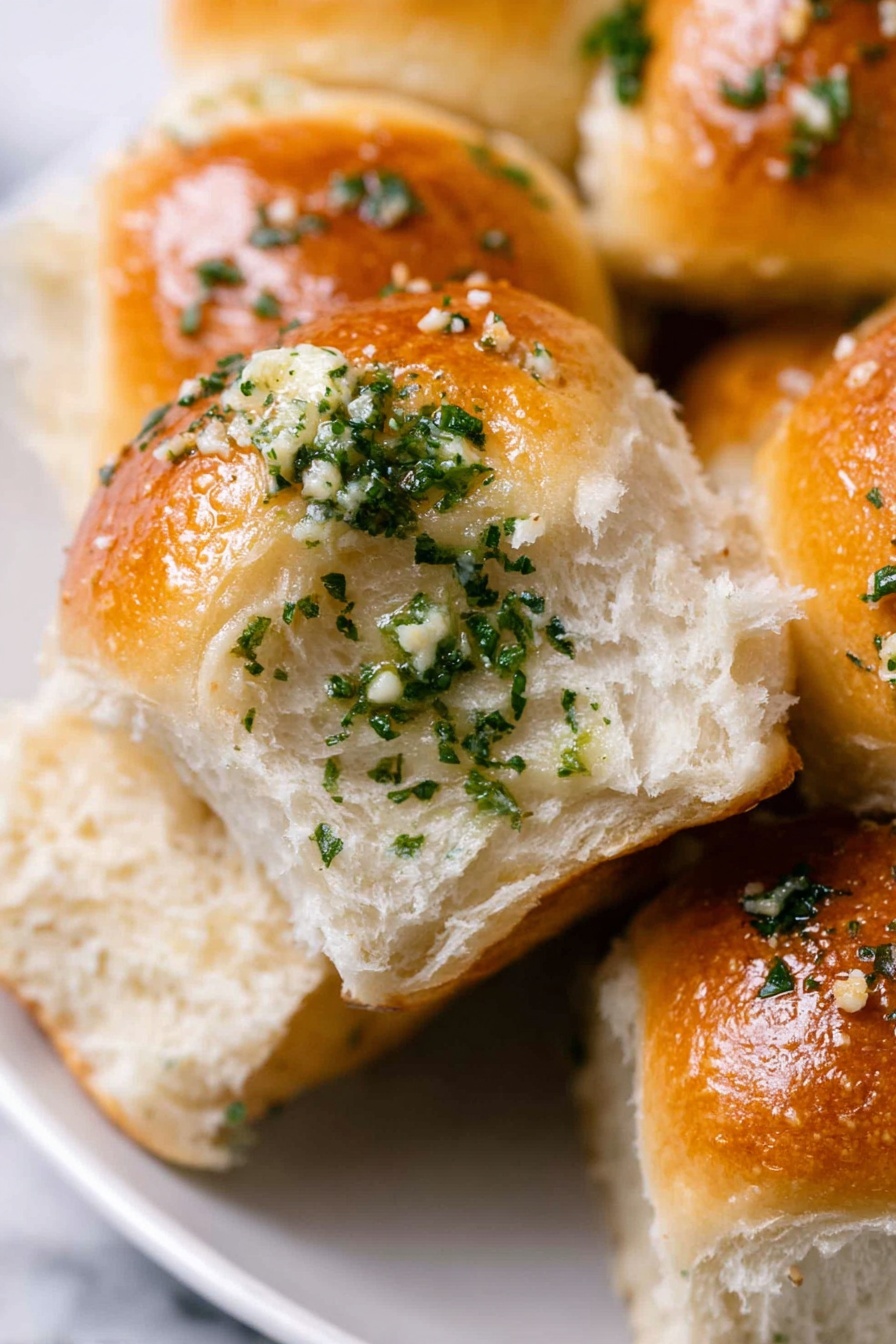 Garlic Bread Rolls, Homemade Garlic Bread, Fluffy Garlic Rolls, Easy Garlic Bread, Soft Bread Rolls - The image shows close-up soft dinner rolls with a shiny golden-brown top layer brushed with garlic butter and small pieces of chopped green herbs, likely parsley, sprinkled generously. The inside of the roll is fluffy and white with a light and airy texture. The rolls are placed closely together on a white plate over a white marbled surface. The focus is on one roll slightly pulled apart to show its soft inside. Photo taken with an iphone --ar 2:3 --v 7