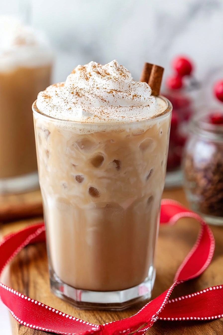 Eggnog White Russian Cocktail, festive eggnog cocktails, holiday White Russian, creamy winter cocktails, eggnog holiday drink - A clear glass is filled almost to the top with a creamy light brown drink. On top, there is a tall, fluffy layer of white whipped cream sprinkled with brown spice. A cinnamon stick is placed in the whipped cream on the right side. The glass sits on a wooden surface, with a folded red ribbon with white stitching lying in front of it. There are some small red berries blurred in the background along with other glass containers. The background has a white marbled texture. photo taken with an iphone --ar 2:3 --v 7