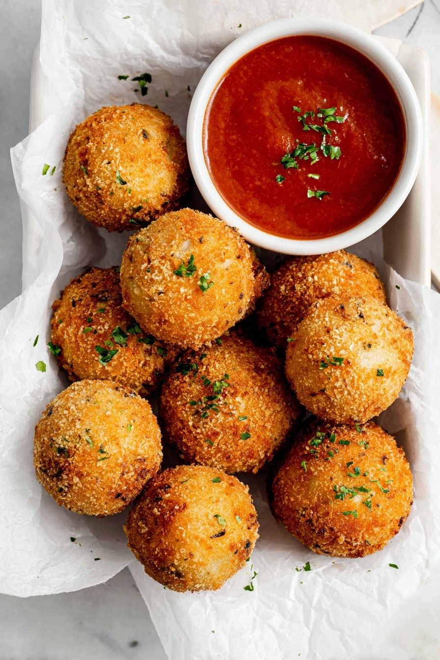 Crispy Potato Cheese Balls, cheesy appetizer recipes, easy snack ideas, crispy potato snacks, mozzarella stuffed potato bites - There are nine golden brown, crispy round balls with a rough texture scattered on white parchment paper inside a white container. Each ball is sprinkled lightly with small bits of green herbs. To the top right of the balls, there is a small white bowl filled with smooth red sauce, garnished with tiny green herb pieces. The background shows a white marbled surface. Photo taken with an iphone --ar 2:3 --v 7