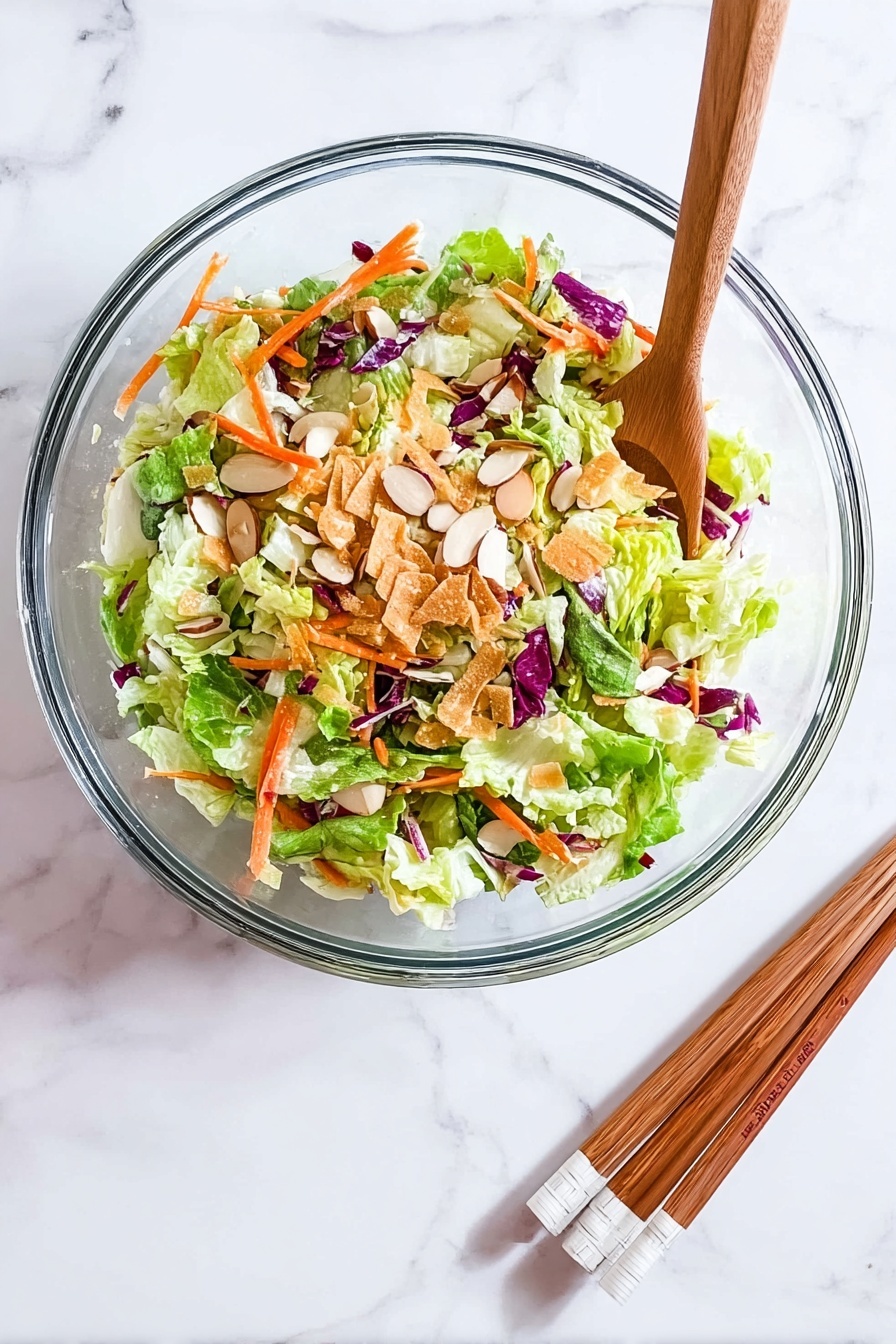 Crispy Asian Chicken Salad Wraps, Asian chicken wraps, crunchy chicken salad, Asian appetizer recipes, easy chicken wraps - A clear glass bowl sits on a white marbled surface, filled with a colorful salad made of several layers: the bottom layer has bright green lettuce leaves mixed with light green cabbage, scattered on top are thin orange carrot strips and bits of purple cabbage, then sprinkled with light brown almond slices and thin crispy golden strips, creating a fresh and crunchy look. Beside the bowl, a pair of wooden chopsticks with white tips rests on the surface. photo taken with an iphone --ar 2:3 --v 7