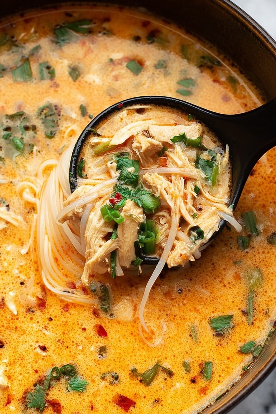 Thai Chicken Curry Soup, Thai Chicken Curry, Chicken Curry Soup, Coconut Curry Soup, Easy Thai Soup - The image shows a close-up of a creamy orange soup with thin white noodles and small pieces of shredded light brown chicken. The soup is garnished with bright green chopped herbs, mostly cilantro and green onions, floating on top. A black ladle holds a scoop of noodles and chicken, partially lifted from the soup. The surface of the soup looks smooth with some specks of black pepper and red chili flakes. The background is a white marbled texture. photo taken with an iphone --ar 2:3 --v 7