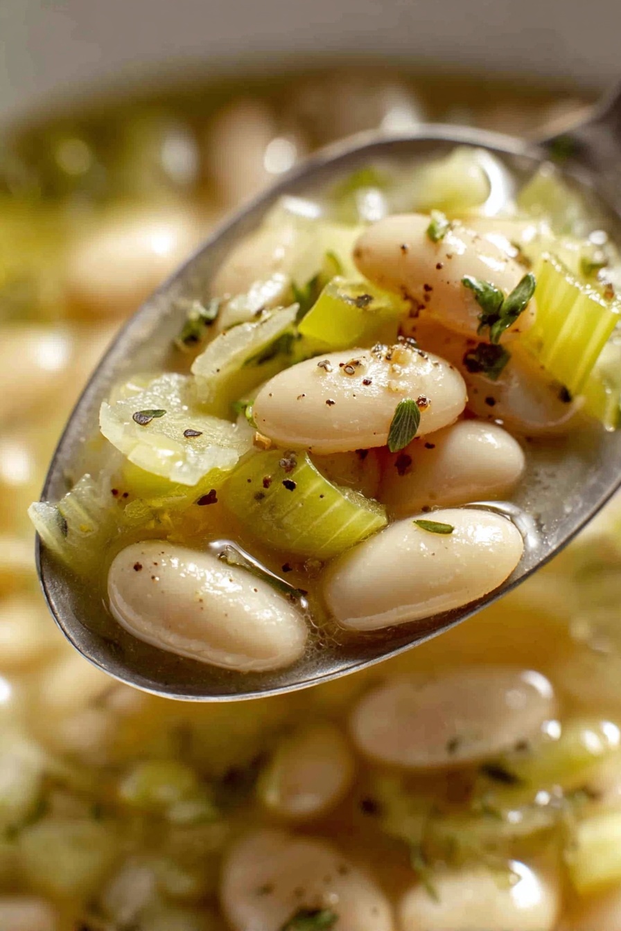 Creamy Butter Bean Leek Skillet, butter bean skillet recipe, leek and butter bean dish, easy creamy vegetable skillet, comforting vegetarian skillet - The image shows a close-up view of a red pot filled with a warm soup made of white beans and chopped green cabbage pieces in a light broth. The beans are smooth and oval-shaped, scattered evenly throughout the soup, while the cabbage is soft and lightly translucent with a pale green color. Small specks of black pepper and fresh thyme sprigs are sprinkled on top for garnish. The pot has a shiny red exterior with a white interior and two handles on the sides. The pot is sitting on a white marbled surface. Photo taken with an iphone --ar 2:3 --v 7