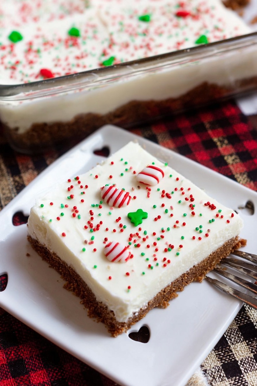 Spiced Gingerbread Cookie Bars, Christmas Dessert Bars, Easy Gingerbread Bars, Holiday Cookie Bars, Warm Spiced Gingerbread Treats - A square dessert bar is shown on a white plate with small heart-shaped cutouts around the edge. The dessert has two clear layers: the bottom layer is a brown, crumbly crust, and the top layer is a thick, smooth, white cream. The white layer is decorated with small round sprinkles in red, green, and white colors, with a pair of white candy pieces with red and green stripes placed near the center. The dessert and plate sit on a wooden surface with a red, black, and beige checkered cloth nearby. Part of a glass baking dish filled with the same dessert and a smiling ceramic cup are visible in the background. A woman's hand holds a fork resting on the plate. photo taken with an iphone --ar 2:3 --v 7