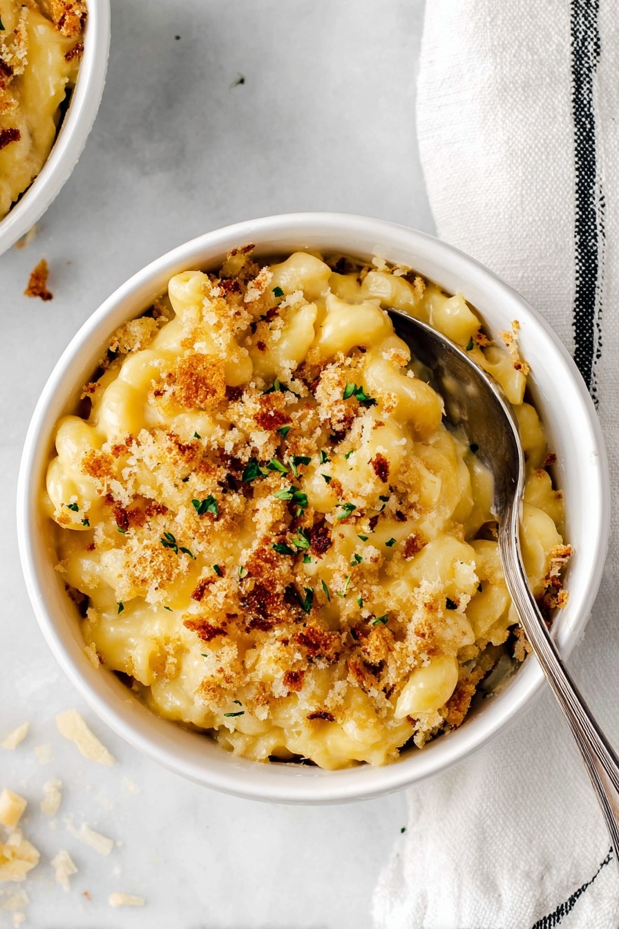 Baked Mac and Cheese with Pretzel Topping, creamy cheesy pasta with crunchy pretzel topping, ultimate baked mac and cheese, cheesy pasta casserole with pretzels, easy baked mac and cheese recipe - A white ceramic casserole dish holds a creamy macaroni and cheese bake with two main layers visible: the bottom thick layer of smooth, pale yellow macaroni pasta coated in rich cheese sauce, and the top layer of golden-brown crispy breadcrumb topping with small green specks sprinkled throughout. A wooden spoon lifts a generous scoop from the dish, showing the creamy macaroni stretching slightly below the crusty layer. The dish sits on a white marbled surface with a clean, bright background. Photo taken with an iphone --ar 2:3 --v 7