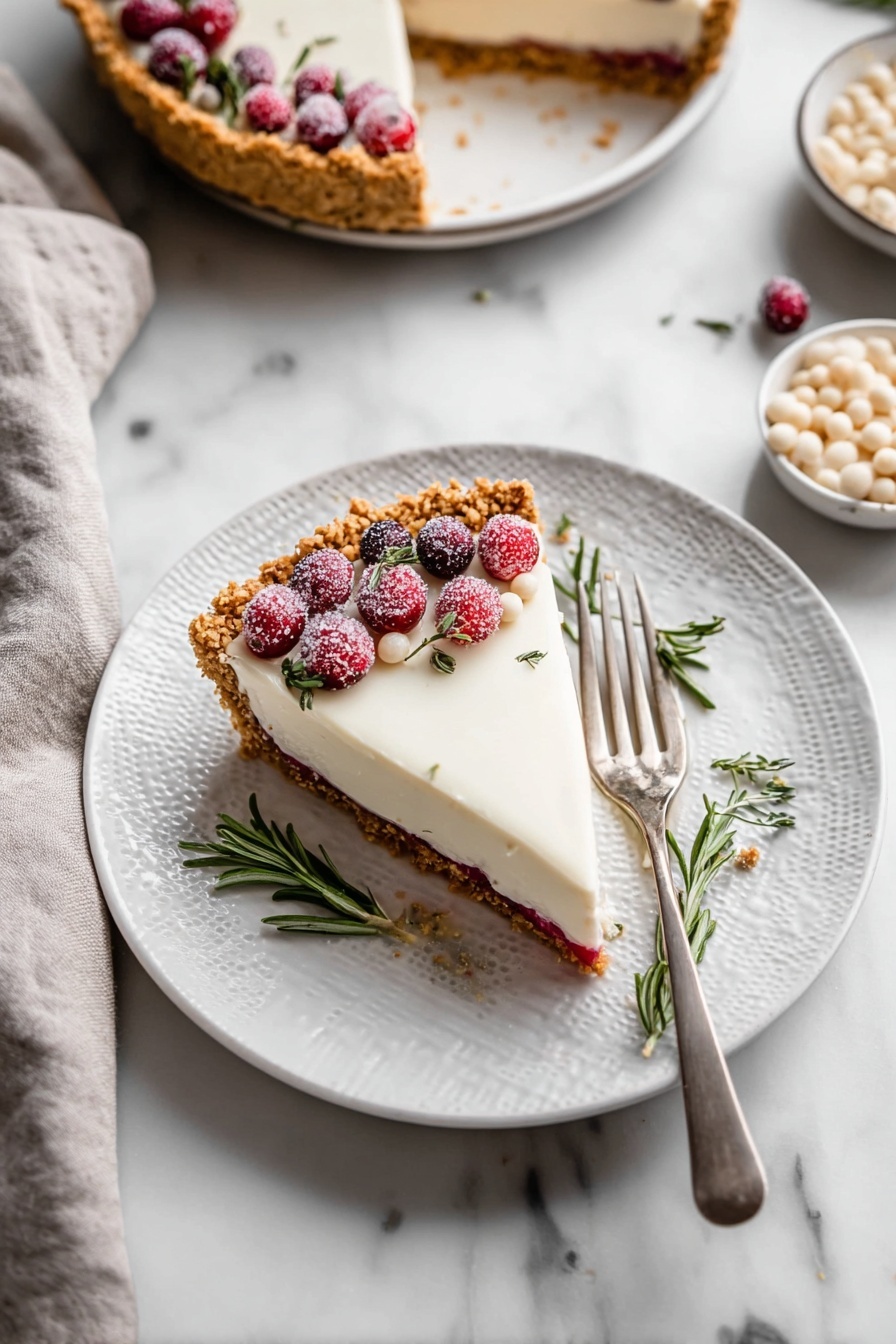 Cranberry White Chocolate Tart, Cranberry White Chocolate Tart Recipe, Holiday Cranberry Tart, White Chocolate Cranberry Dessert, Elegant Tart Recipes - The image shows a slice of pie on a white plate with a textured rim, placed on a white marbled surface. The pie has three visible layers: a golden brown crumbly crust, a thin red layer in the middle, and a thick, smooth white topping. The slice is decorated on one side with sugared red cranberries, a few small white drops, and sprigs of fresh green rosemary. A silver fork rests on the right side of the plate. Nearby, there is a whole pie with a similar topping and decoration, and a bowl filled with small white drops. A light gray cloth is placed towards the bottom left corner of the image. Photo taken with an iphone --ar 2:3 --v 7