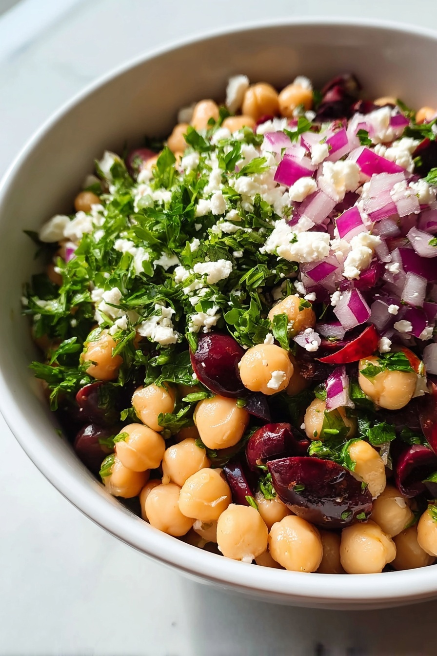 Chickpea Black Bean Salad, Chickpea Black Bean Salad recipe, healthy chickpea black bean salad, easy vegetarian bean salad, protein-rich bean salad - A close-up view of a white bowl filled with a colorful chickpea salad, showing roughly three layers. The bottom layer consists of smooth, round pale beige chickpeas mixed with dark purple olives. The middle layer has bright green chopped leaves, likely parsley, scattered throughout. The top layer is dotted with small white cheese crumbles and chopped purple-red onions, adding texture and vibrant color contrast. The bowl sits on a white marbled surface. photo taken with an iphone --ar 2:3 --v 7