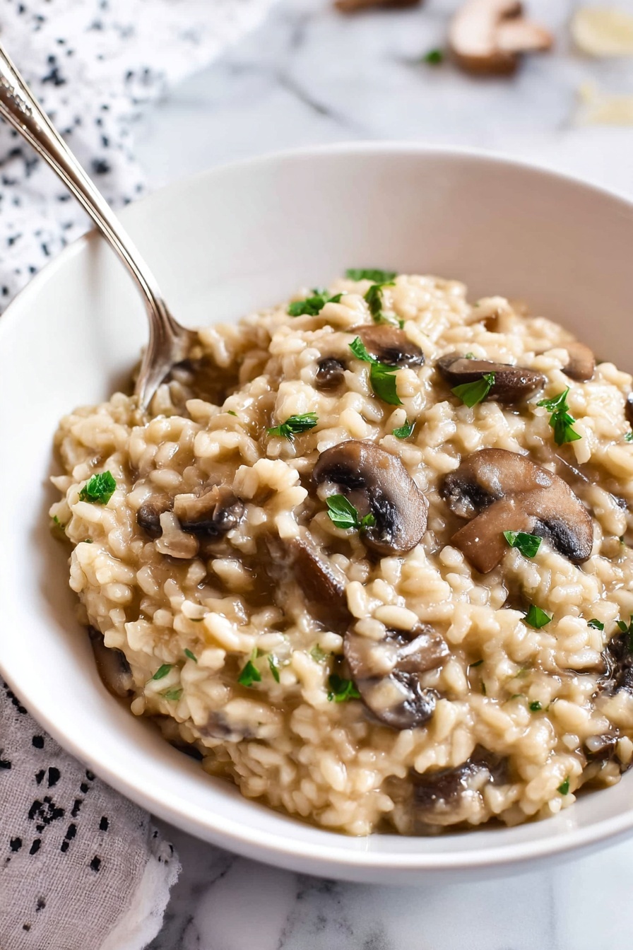 Pressure Cooker Mushroom Risotto, quick mushroom risotto, creamy mushroom risotto, easy pressure cooker recipes, vegetarian pressure cooker dishes - A white bowl filled with creamy mushroom risotto. The risotto has a thick, soft texture with plump, tender rice grains mixed with sliced brown mushrooms. Small pieces of green herbs are sprinkled on top, adding color contrast. A silver spoon is partially dipped into the risotto, resting near the edge of the bowl. The bowl sits on a white marbled surface with part of a white and black patterned cloth visible in the background. Photo taken with an iphone --ar 2:3 --v 7
