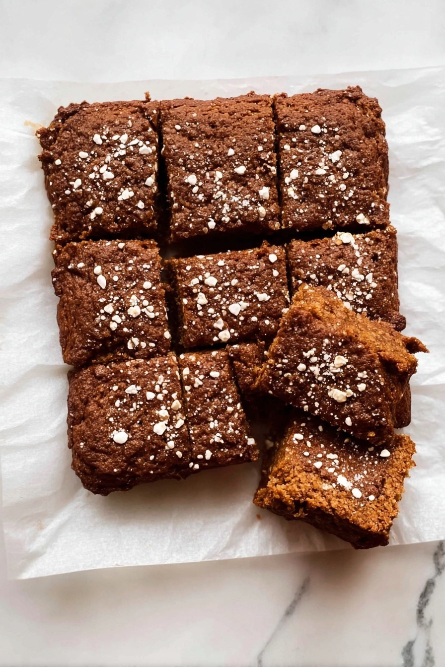 Healthy Apple Oatmeal Cake, gluten-free apple oatmeal dessert, nourishing breakfast cake, flourless apple cake recipe, healthy apple cinnamon treat - The dish is a rectangular brown baked cake cut into nine pieces with a rough texture and a slightly cracked top. The cake is sprinkled with white oat flakes spread unevenly over the surface. It rests on white parchment paper placed on a white marbled surface. One piece in the top right corner is separated from the rest, showing the inside of the cake, which is soft and dense with a uniform brown color. photo taken with an iphone --ar 2:3 --v 7