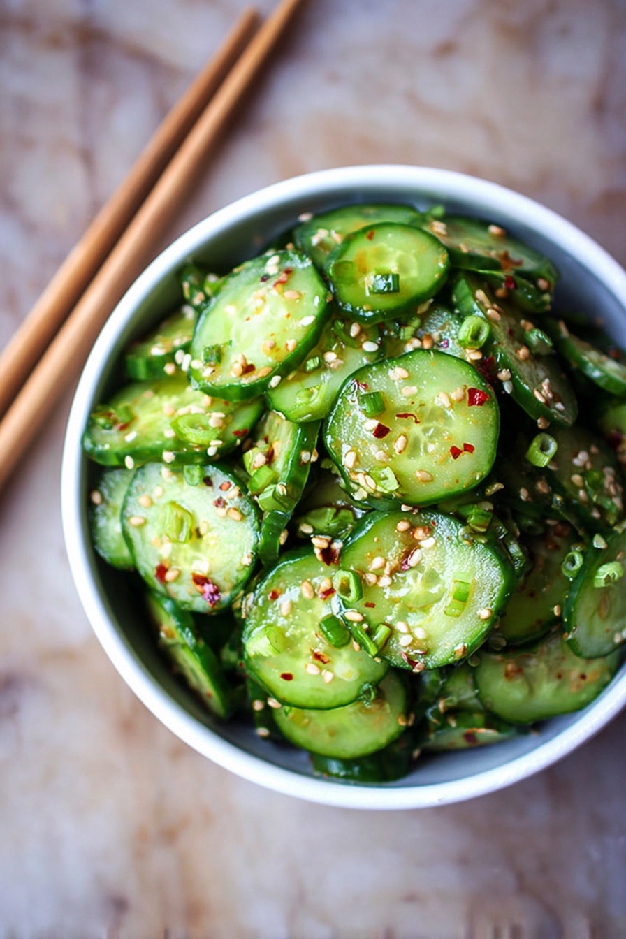Asian Cucumber Salad, cucumber salad recipe, Asian side dish, crunchy cucumber salad, quick healthy salad - A white bowl filled with many thin, round slices of cucumber with bright green skins and a glossy texture from light dressing, topped with small white sesame seeds and small pieces of green onion mixed in. The cucumbers are stacked to create a small mound that rises above the bowl. The bowl has small brown spots and is placed on a wooden surface with a pair of light brown chopsticks laying beside it. The background is dark and out of focus. photo taken with an iphone --ar 2:3 --v 7