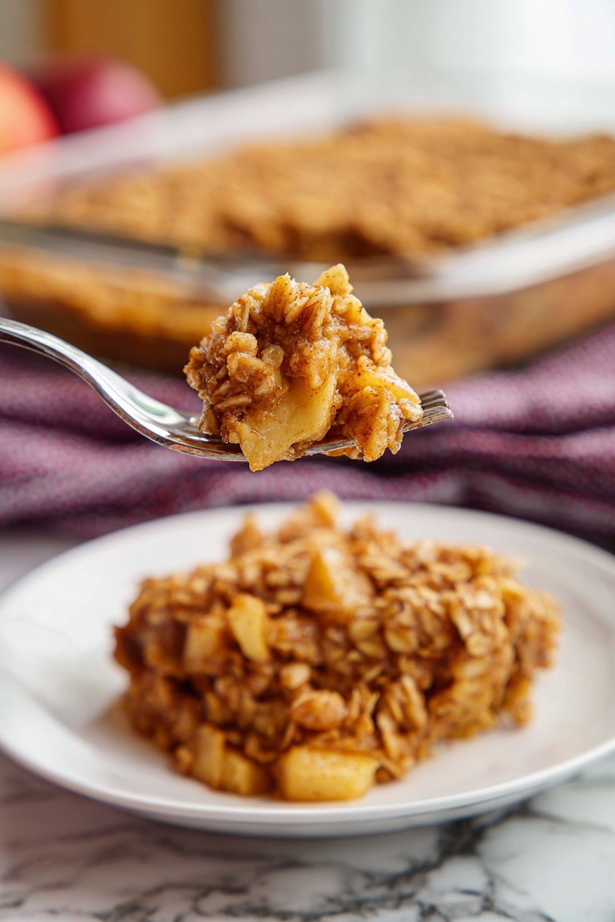 Apple Cinnamon Baked Oatmeal, healthy baked oatmeal, cozy breakfast recipes, easy baked oatmeal with apples, cinnamon oatmeal breakfast - A single square piece of oat crumble dessert sits in the center of a white plate with ridged edges. The dessert has two main layers: the top layer is golden brown with a rough texture made of baked oats mixed with cinnamon, while the bottom layer appears softer and darker, showing a moist filling beneath the oats. The plate is placed on a wooden table, and in the background, there is a glass baking dish with more of the same oat crumble. A dark red and white checkered cloth is also slightly visible behind the plate. Photo taken with an iphone --ar 2:3 --v 7