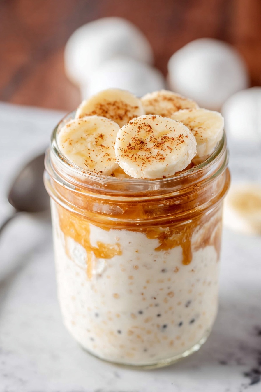 Peanut Butter Banana Overnight Oats, healthy breakfast recipes, quick overnight oats, easy breakfast ideas, banana oatmeal jar - A clear glass jar with a silver metal lid filled with three layers of overnight oats. The bottom layer is creamy white with tiny pieces of oats and seeds showing through. The middle layer has a light brown chunk inside the creamy oats mixture creating a rough texture. The top layer blends smoothly into the silver lid. The jar sits on a white marbled surface with scattered oats around, a white cloth on the left, and a yellow banana on the right photo taken with an iphone --ar 2:3 --v 7