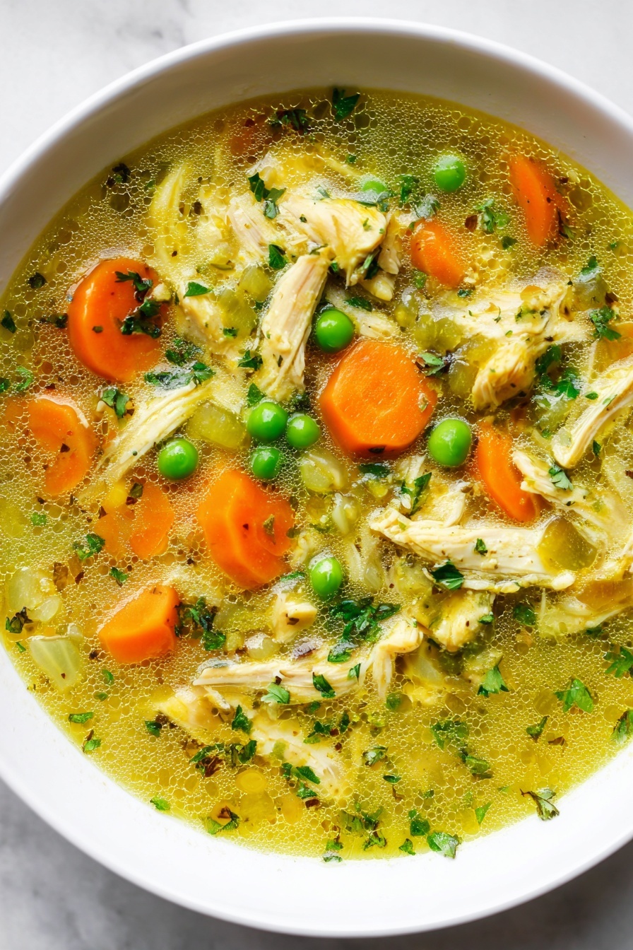 Turmeric Chicken Soup, healthy turmeric soup, anti-inflammatory soup, comforting chicken soup, golden turmeric broth - A close-up view of a white bowl filled with chicken soup. The soup has many layers: on top are bright orange carrot slices, green peas, and pale green celery pieces mixed with shredded light yellow chicken. The broth is clear with a yellow tint and small green herb bits floating throughout. There is a silver spoon resting in the soup, with a woman's hand holding the spoon near the edge of the bowl. The bowl is placed on a white marbled surface. Photo taken with an iphone --ar 2:3 --v 7