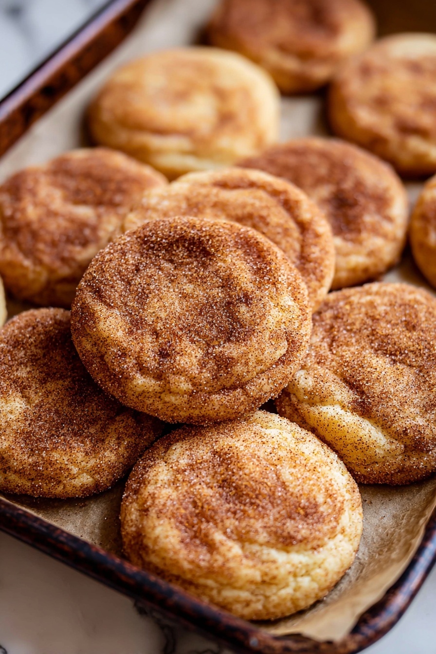 Chewy Snickerdoodle Cookies, cinnamon sugar cookies, soft chewy snickerdoodles, classic snickerdoodle recipe, best snickerdoodle cookies - A close-up top view of soft round cookies on a white marbled surface with some cookies dusted in a cinnamon-sugar mix showing a light brown texture and others showing a darker brown cinnamon coating. In the foreground, a white bowl is half-filled with cinnamon sugar, with one cookie being dipped halfway inside, showing a mix of light and darker brown swirls from the coating. The cookies have a slightly cracked, soft surface texture. photo taken with an iphone --ar 2:3 --v 7