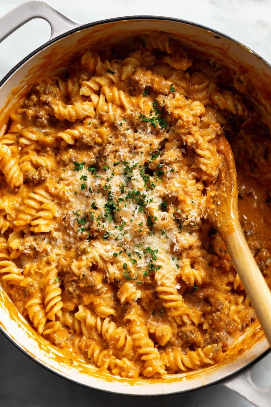 Creamy Tomato Beef Pasta, hearty beef pasta, creamy pasta recipes, quick weeknight pasta, one-pot beef pasta - A large white pot filled with twisted rotini pasta covered in a thick, creamy orange sauce mixed with small bits of browned meat. The pasta is well coated and there is a sprinkle of grated cheese and chopped green herbs on top. A wooden spoon is seen stirring the pasta from the right side. The pot sits on a white marbled surface. photo taken with an iphone --ar 2:3 --v 7